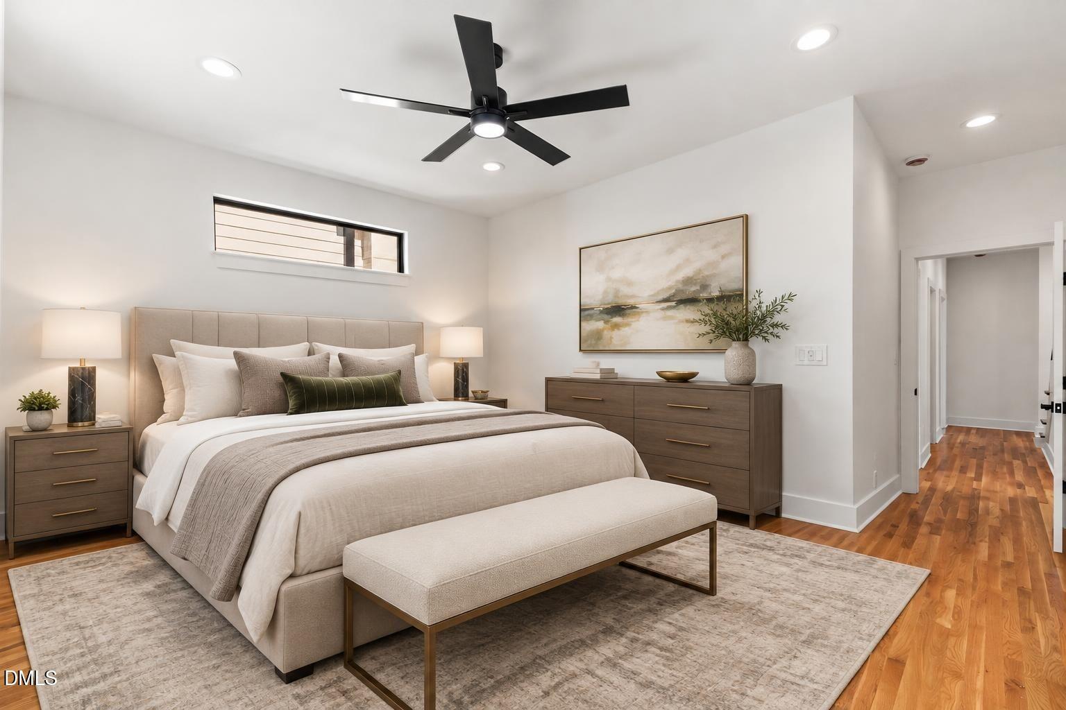 Staged bedroom with a large upholstered bed, neutral bedding, black ceiling fan, and hardwood floors.