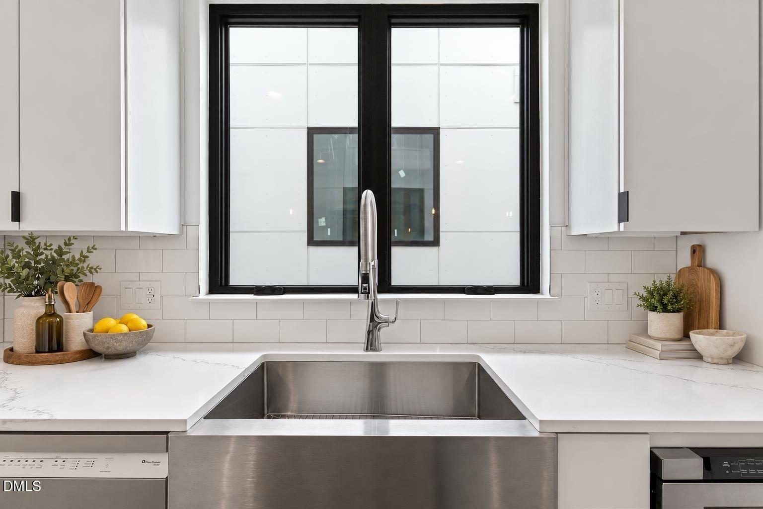 Modern kitchen with a stainless farmhouse sink beneath a black-framed window and white veined countertops.