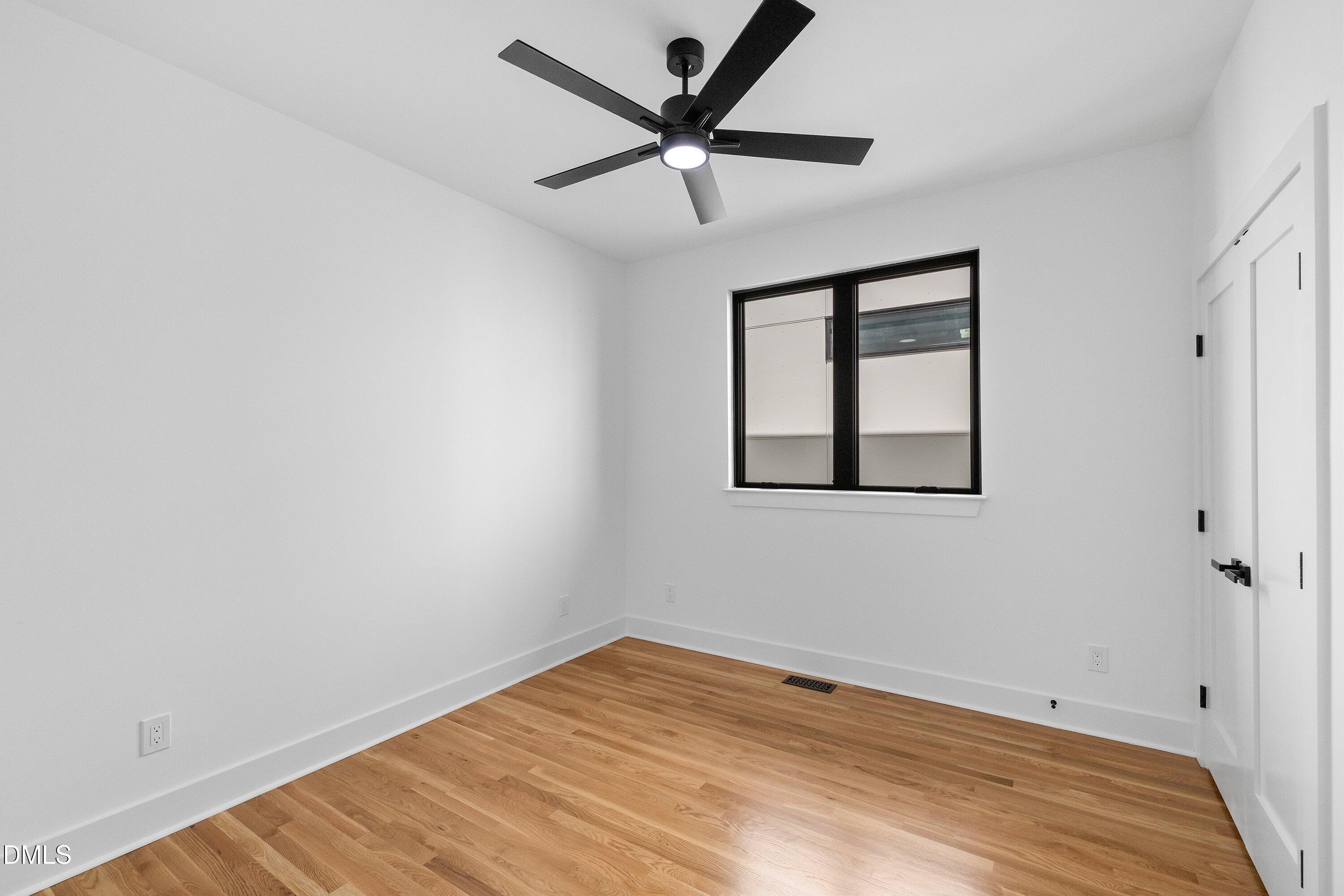 Empty room with light oak floors, a black-framed window, and a ceiling fan with light.