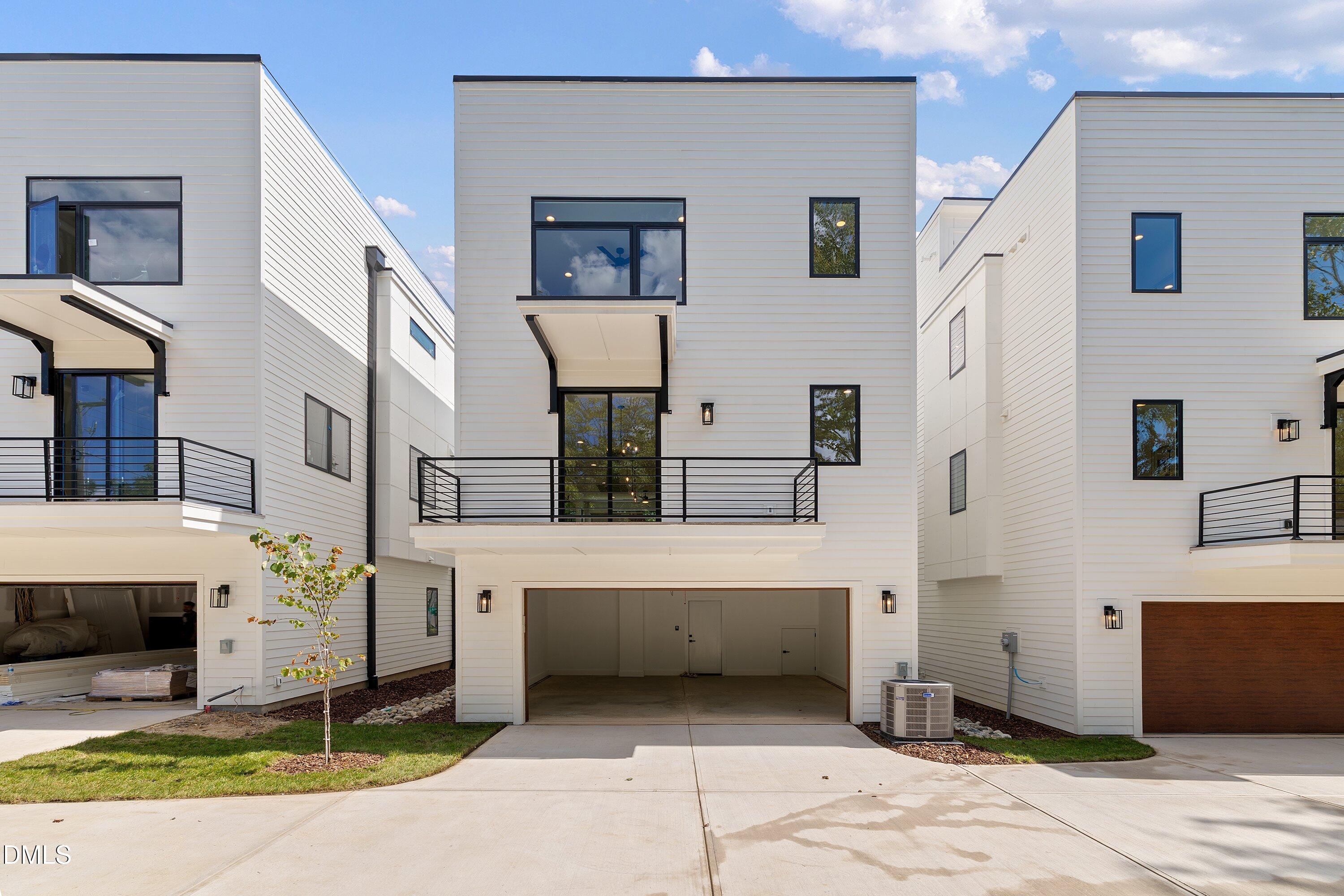 Modern white townhouse with a second-floor balcony and open garage, flanked by similar homes.