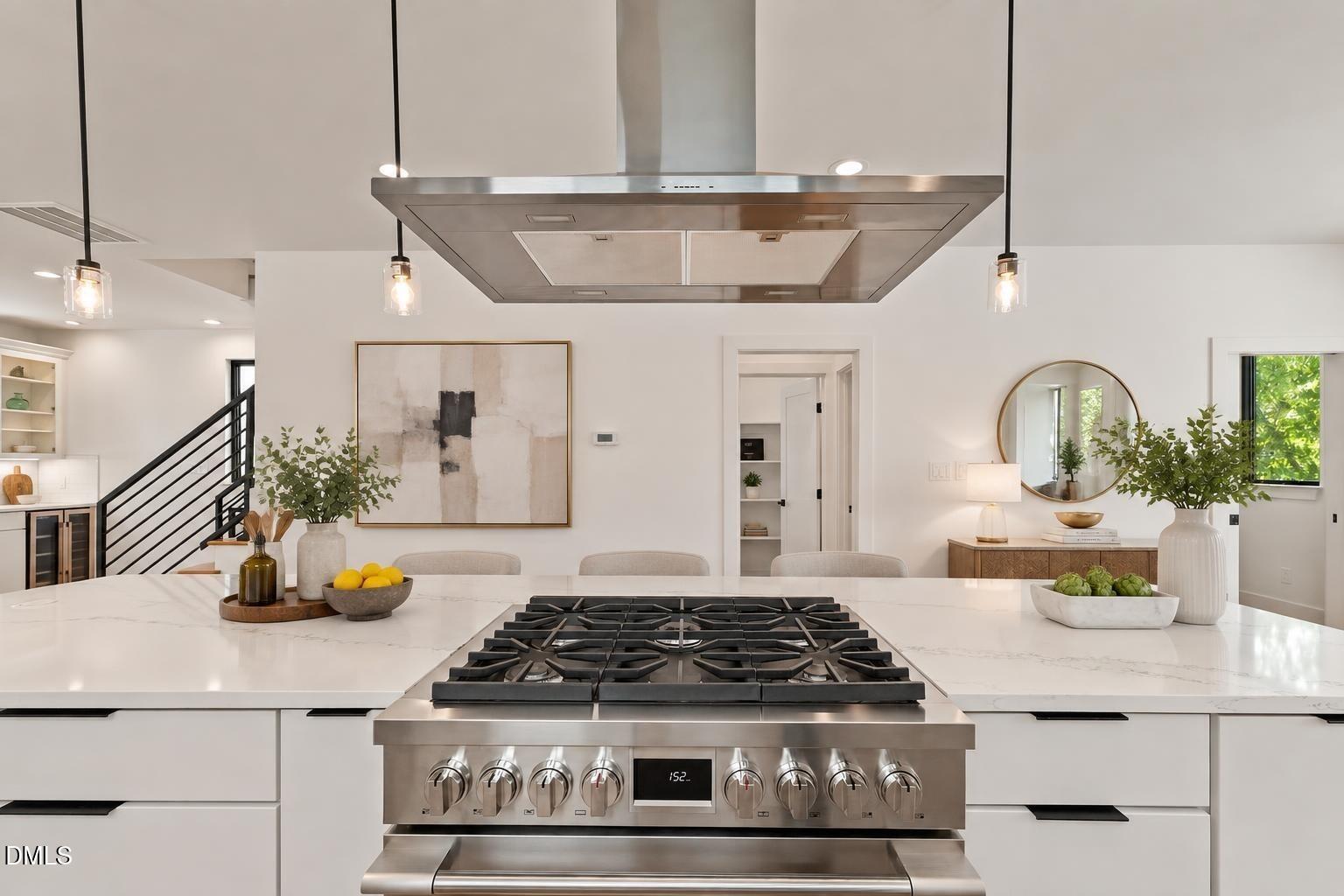 Modern kitchen with a marble island, prominent stainless-steel gas range, and black metal staircase.