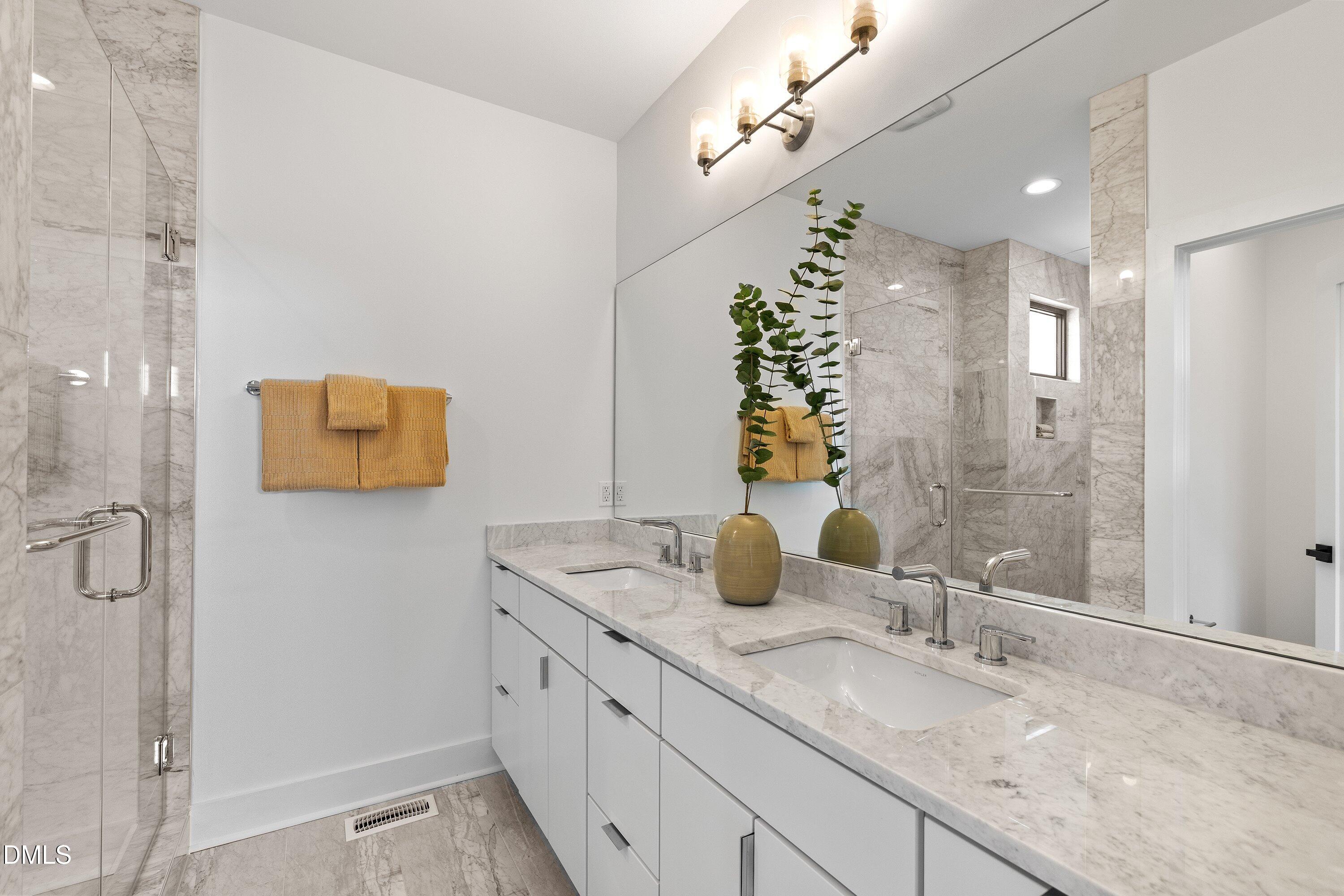 Bathroom with a marble double vanity, expansive mirror, and glass-enclosed marble shower.