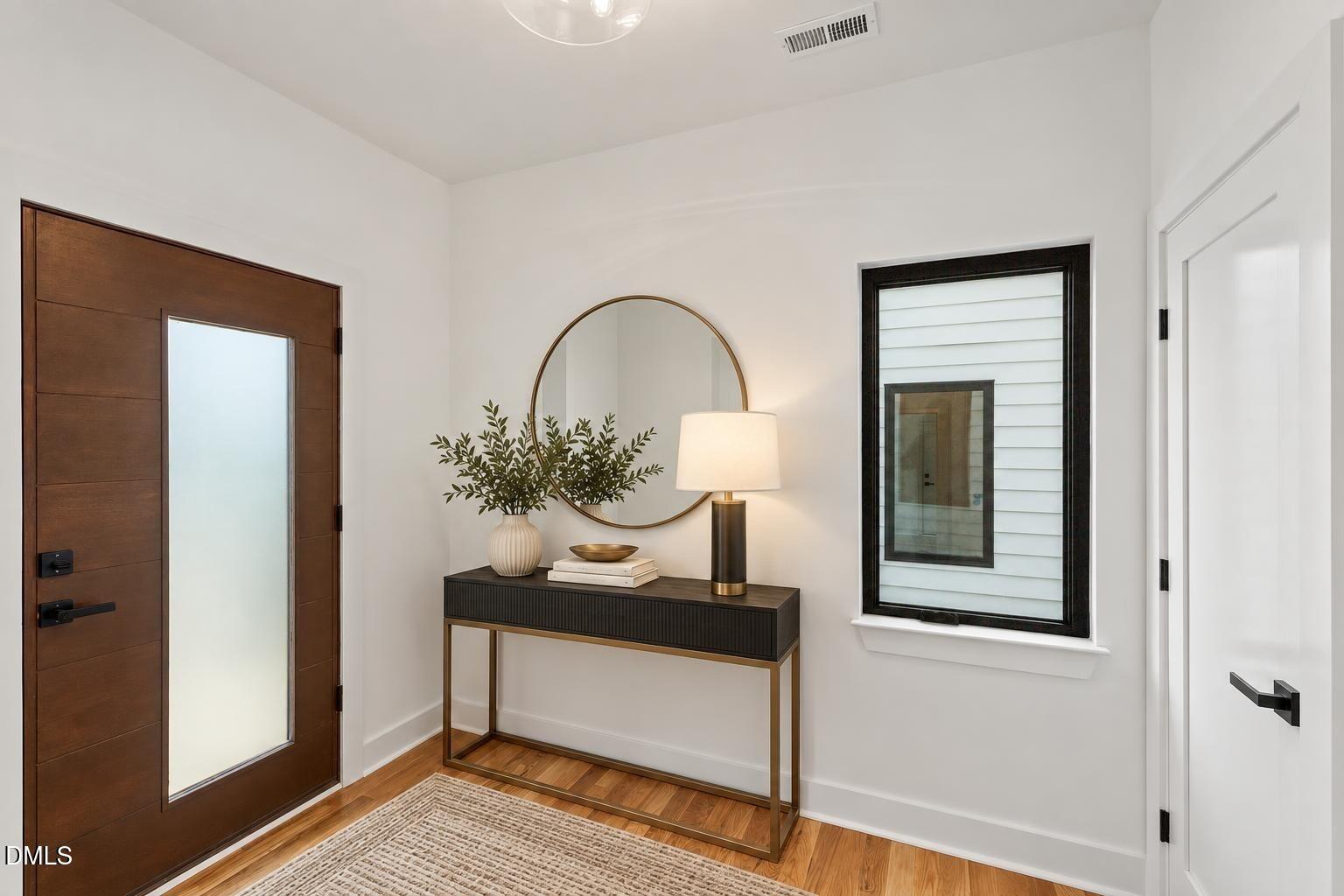 Entry foyer with a dark wood and frosted-glass front door, console table, round mirror, and hardwood floors.