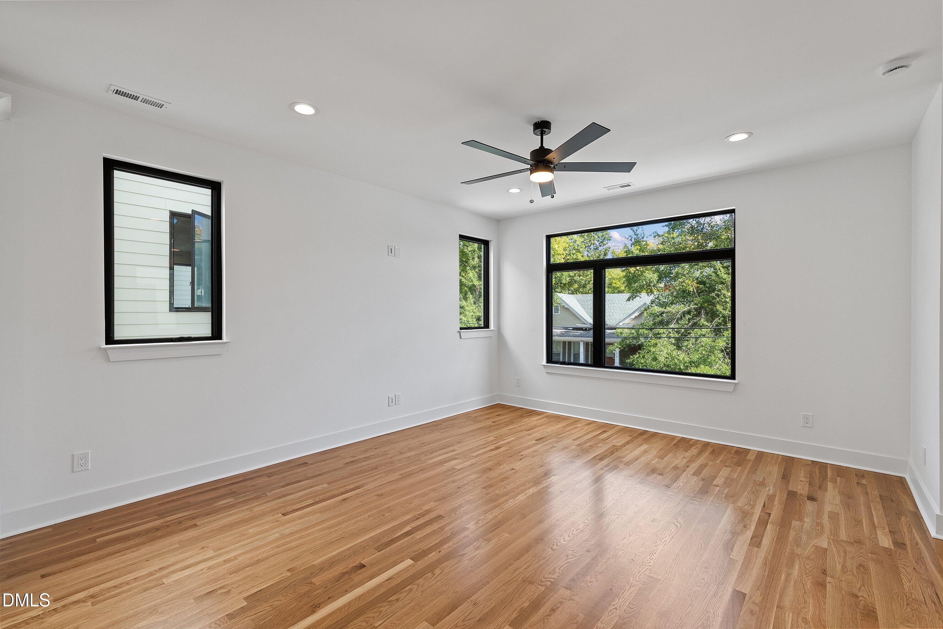 Empty room with hardwood floors, large black-framed windows, and a ceiling fan.