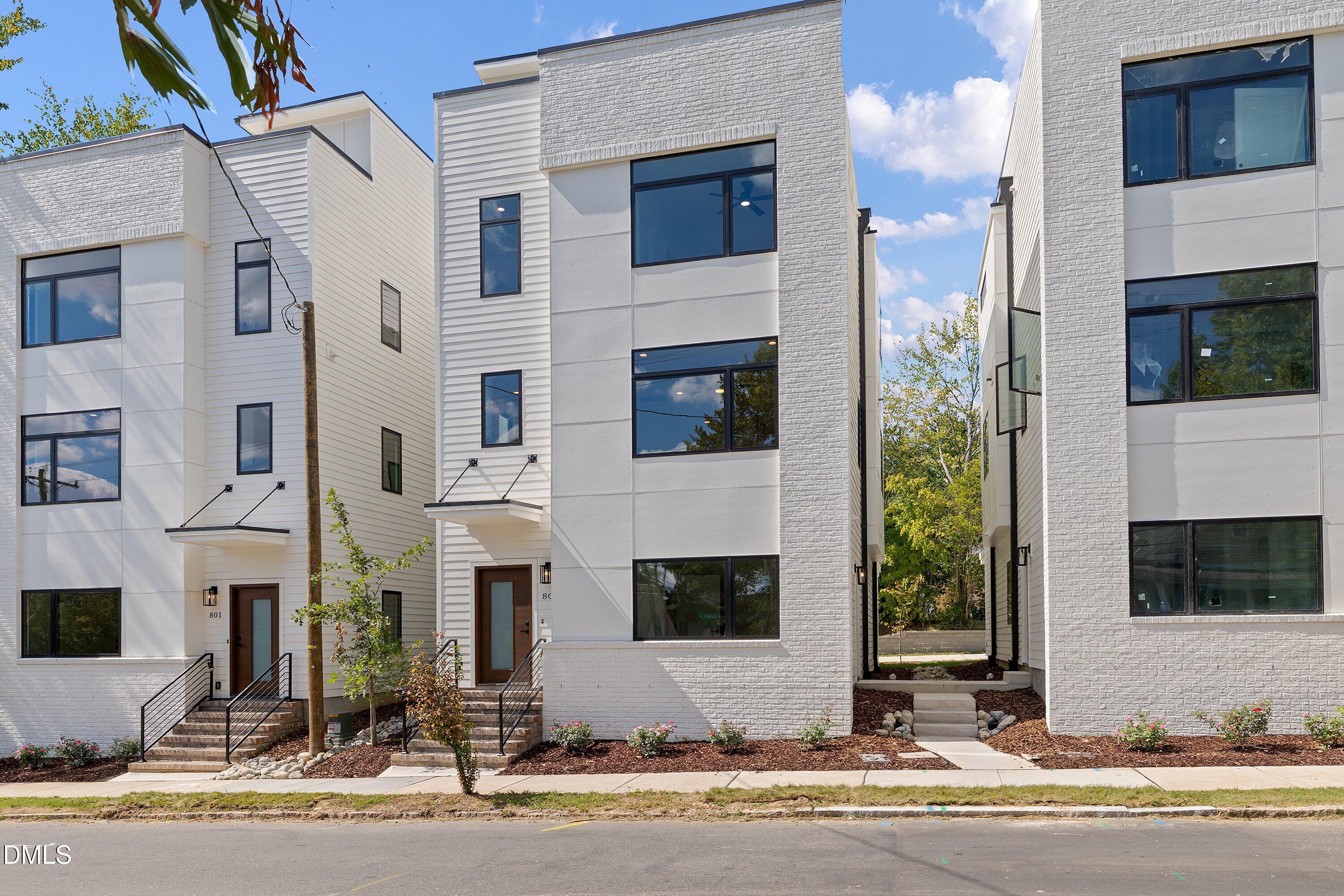 Modern white townhouses with black-framed windows, brick accents, and landscaped front entries.