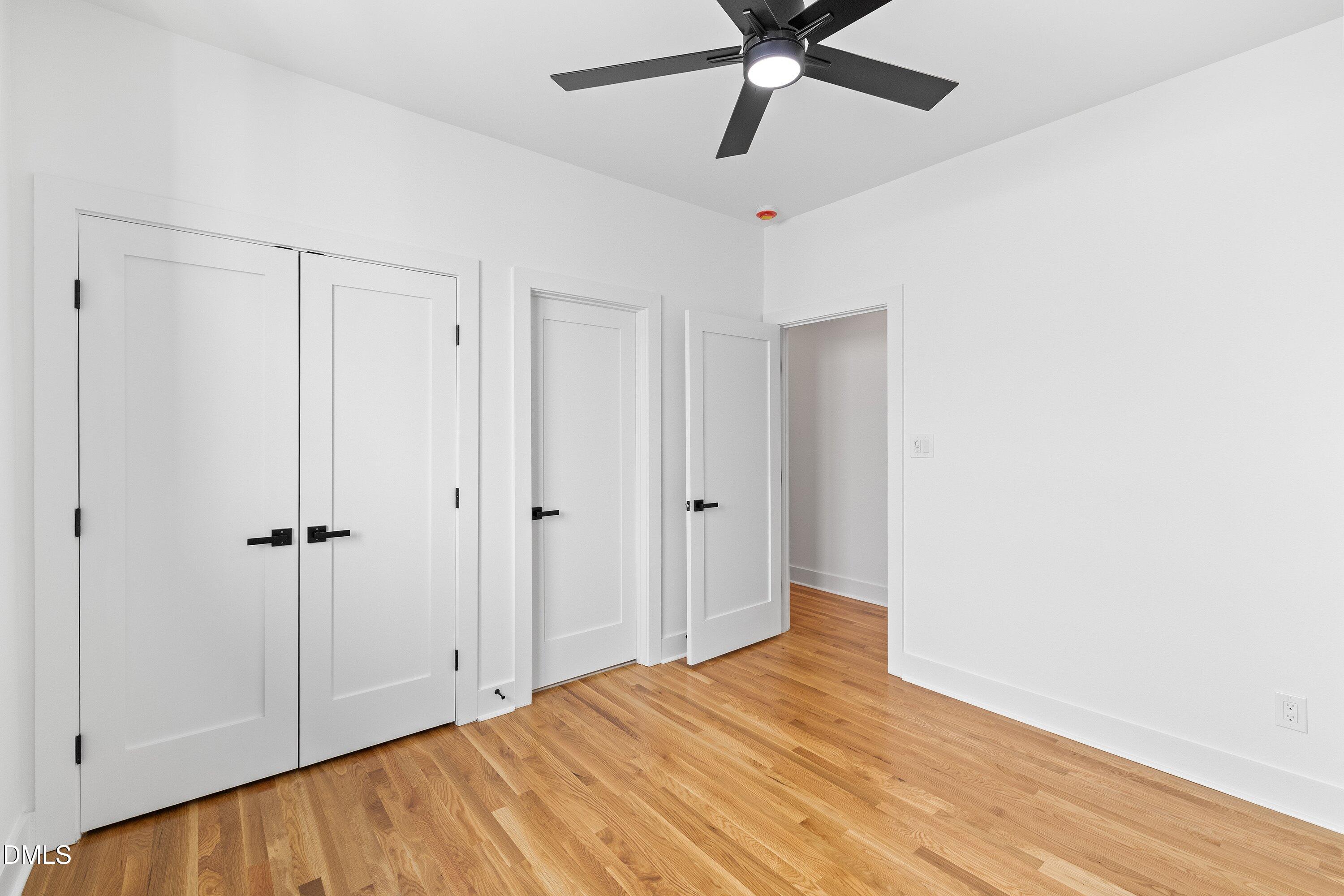 Unfurnished room with hardwood floors, white paneled doors, and a black ceiling fan.