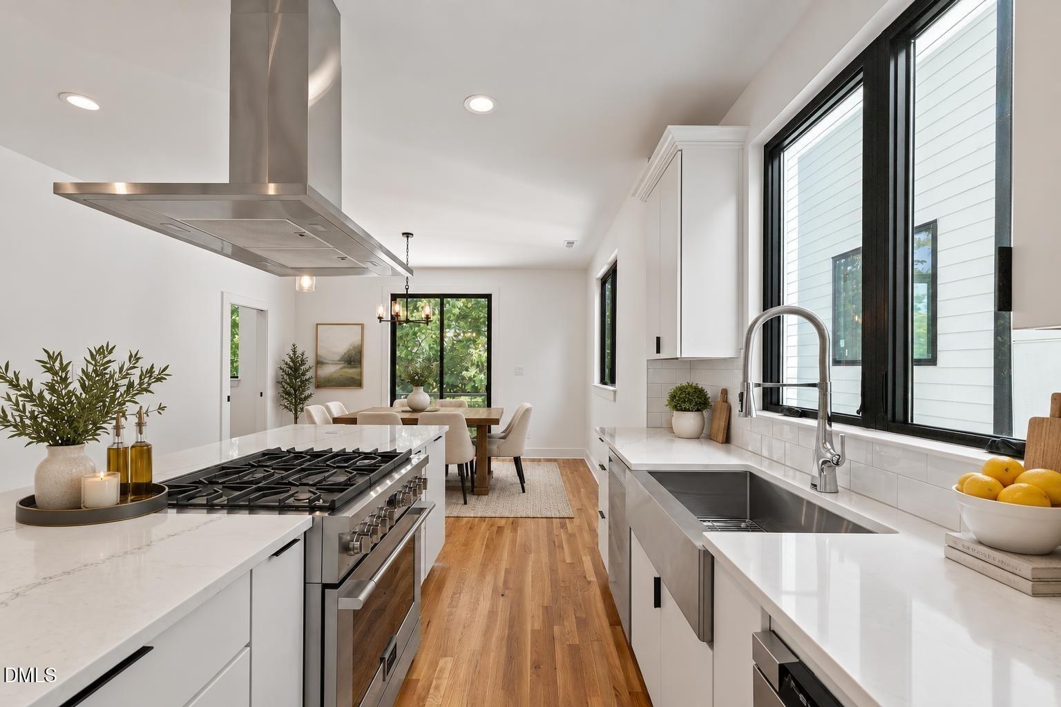 Bright white kitchen with marble counters, a stainless steel range, and black-framed windows.