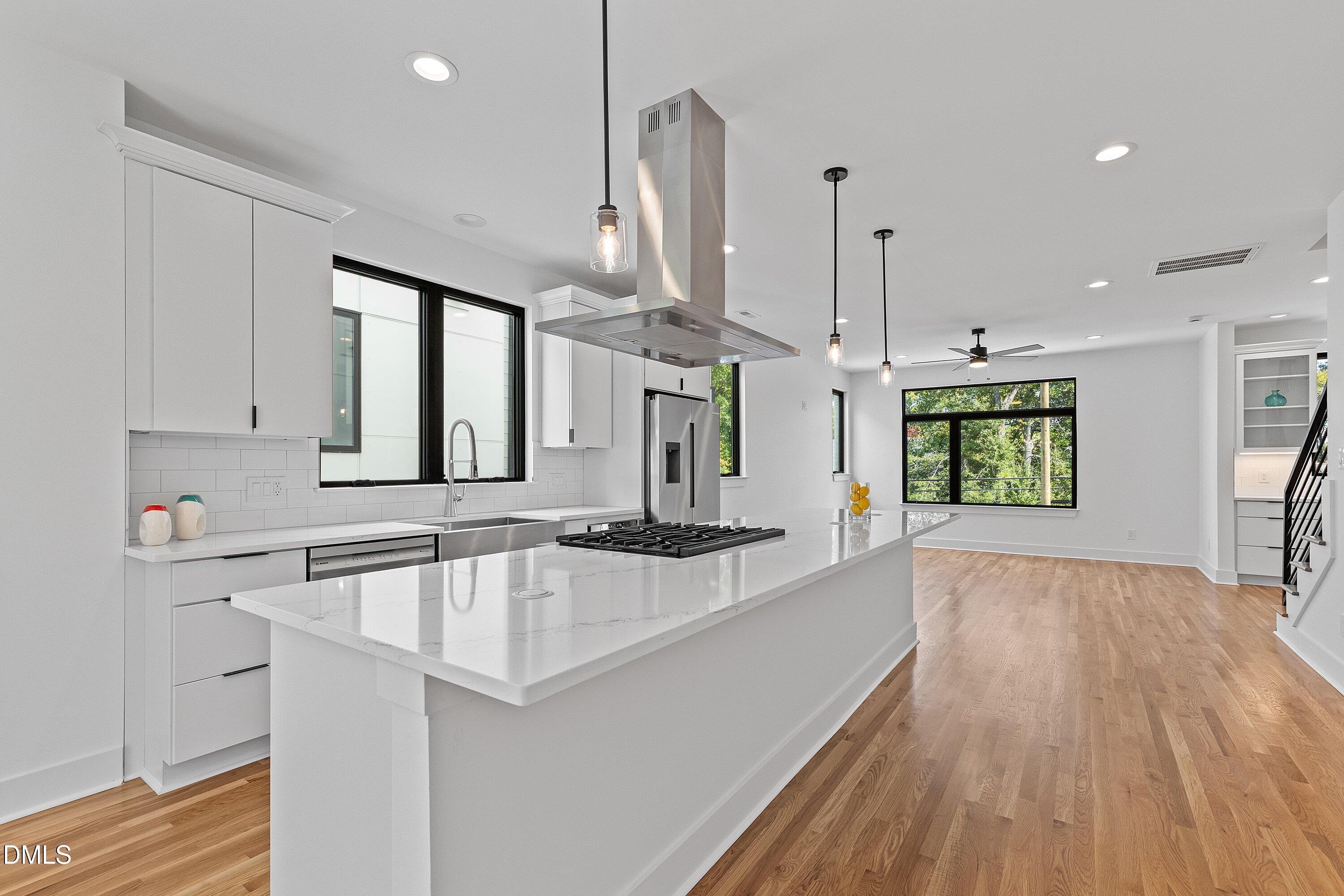 Modern white kitchen with a large quartz island, stainless steel range hood, and hardwood floors.