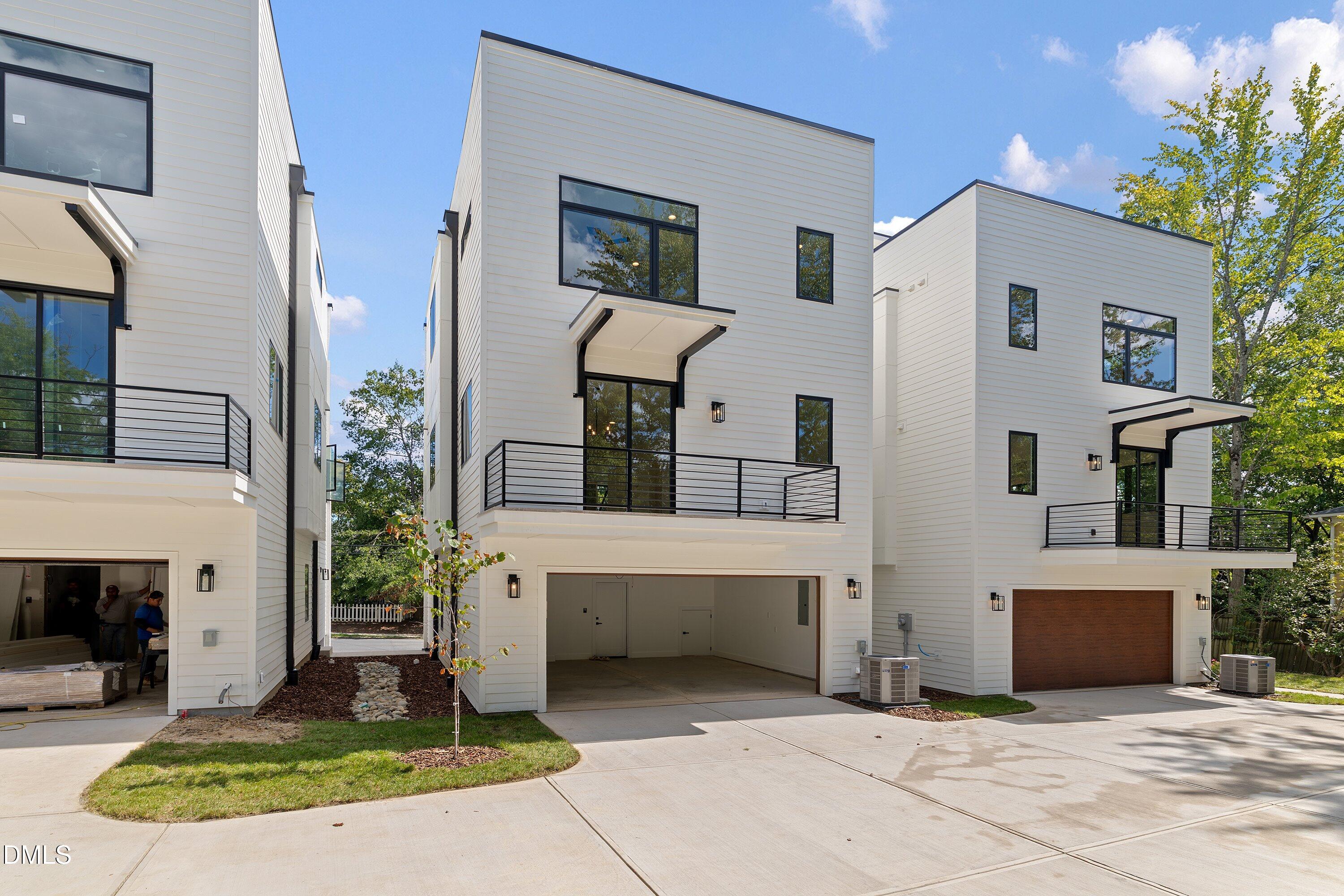 Modern white attached homes with balconies, black-framed windows, and open ground-level garages.