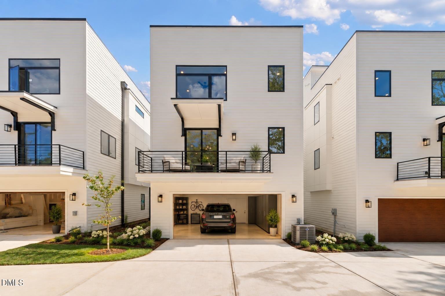 Modern white townhouse with a second-floor balcony, open garage, and landscaped front yard.