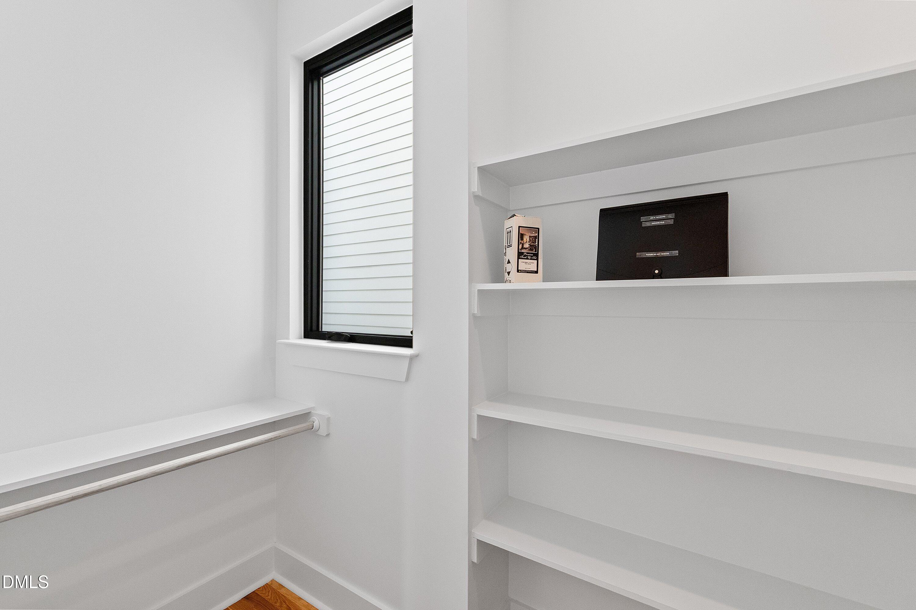 Walk-in closet with built-in shelving, a hanging rod, and a black-trimmed window.