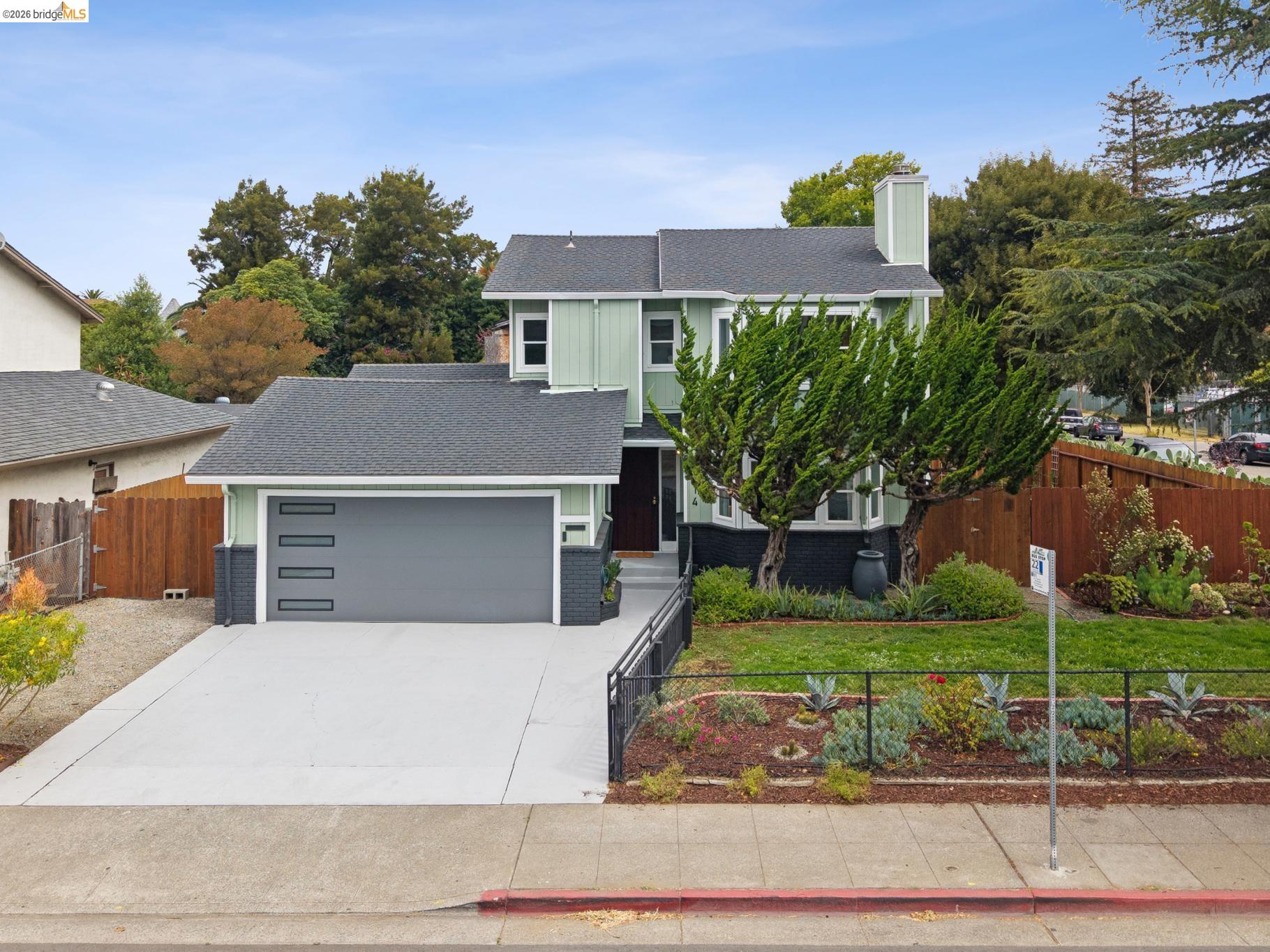 Two-story pale green house with an attached garage, broad driveway, and landscaped yard.