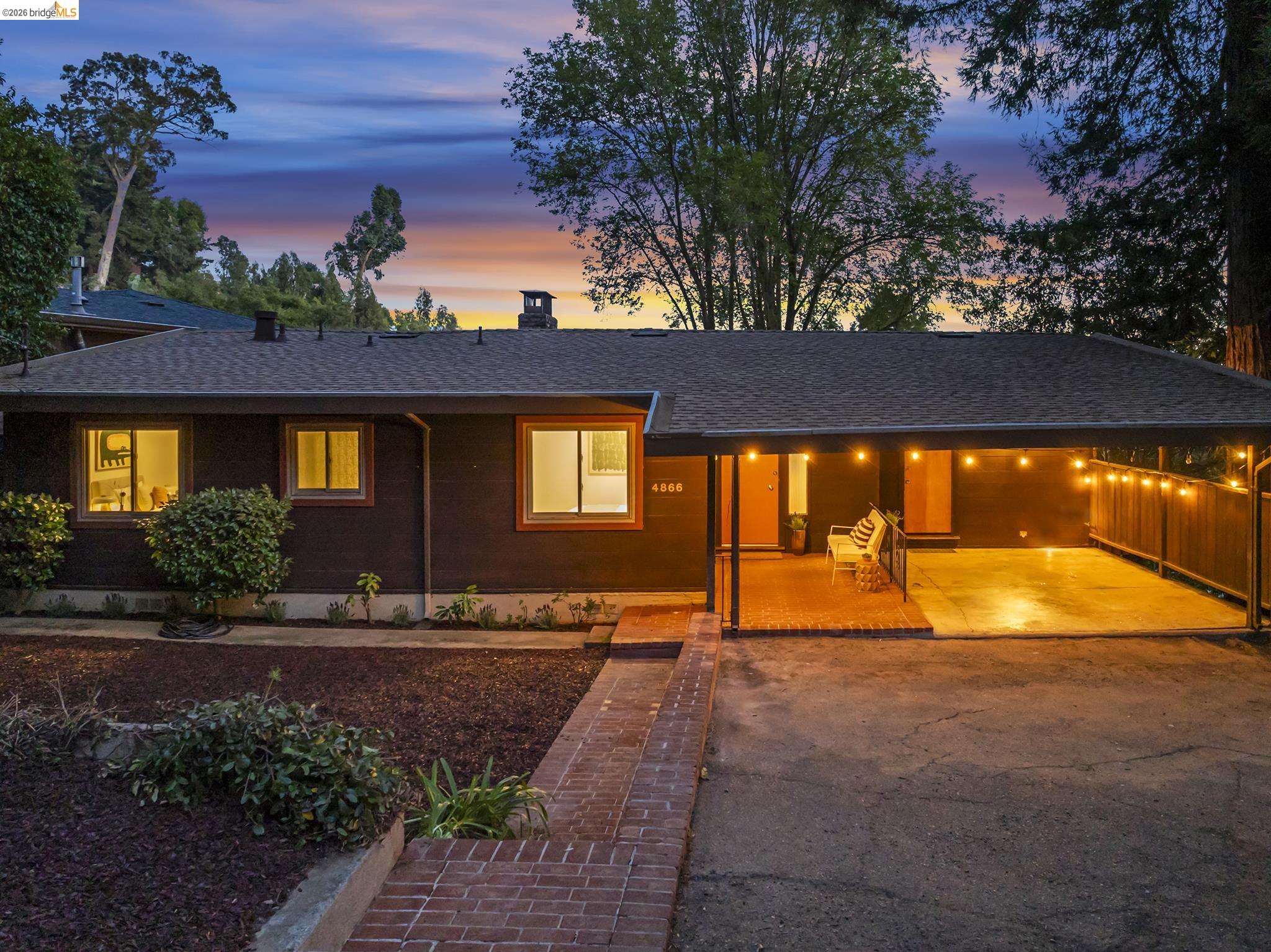 Single-story home at dusk with a warmly lit covered carport and brick walkway.