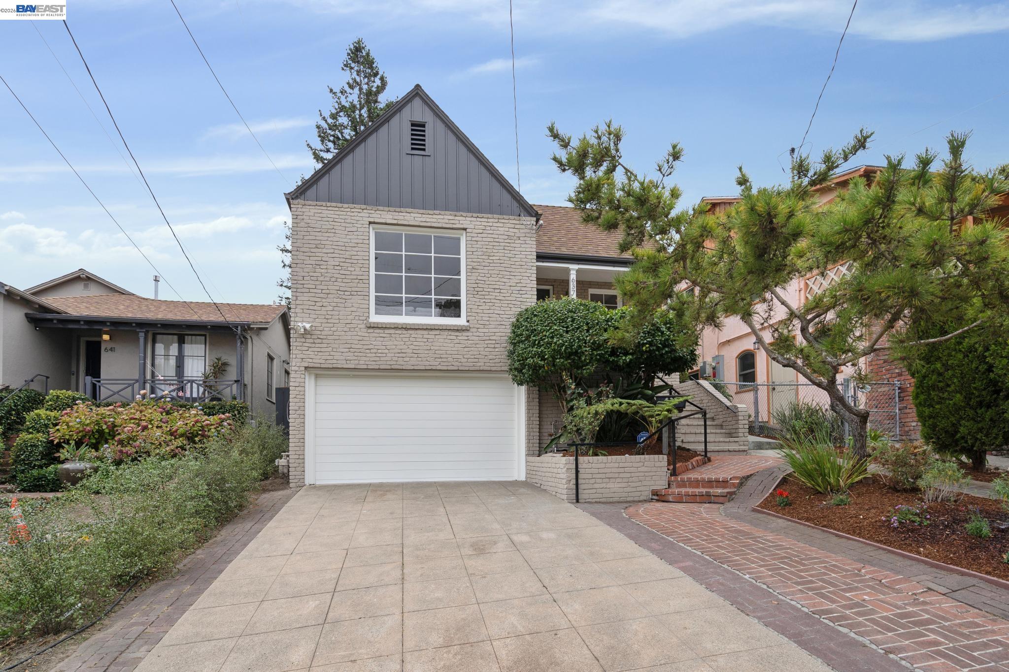 Light brick home with a steep gray gable, white garage door, broad driveway, and landscaped front yard.
