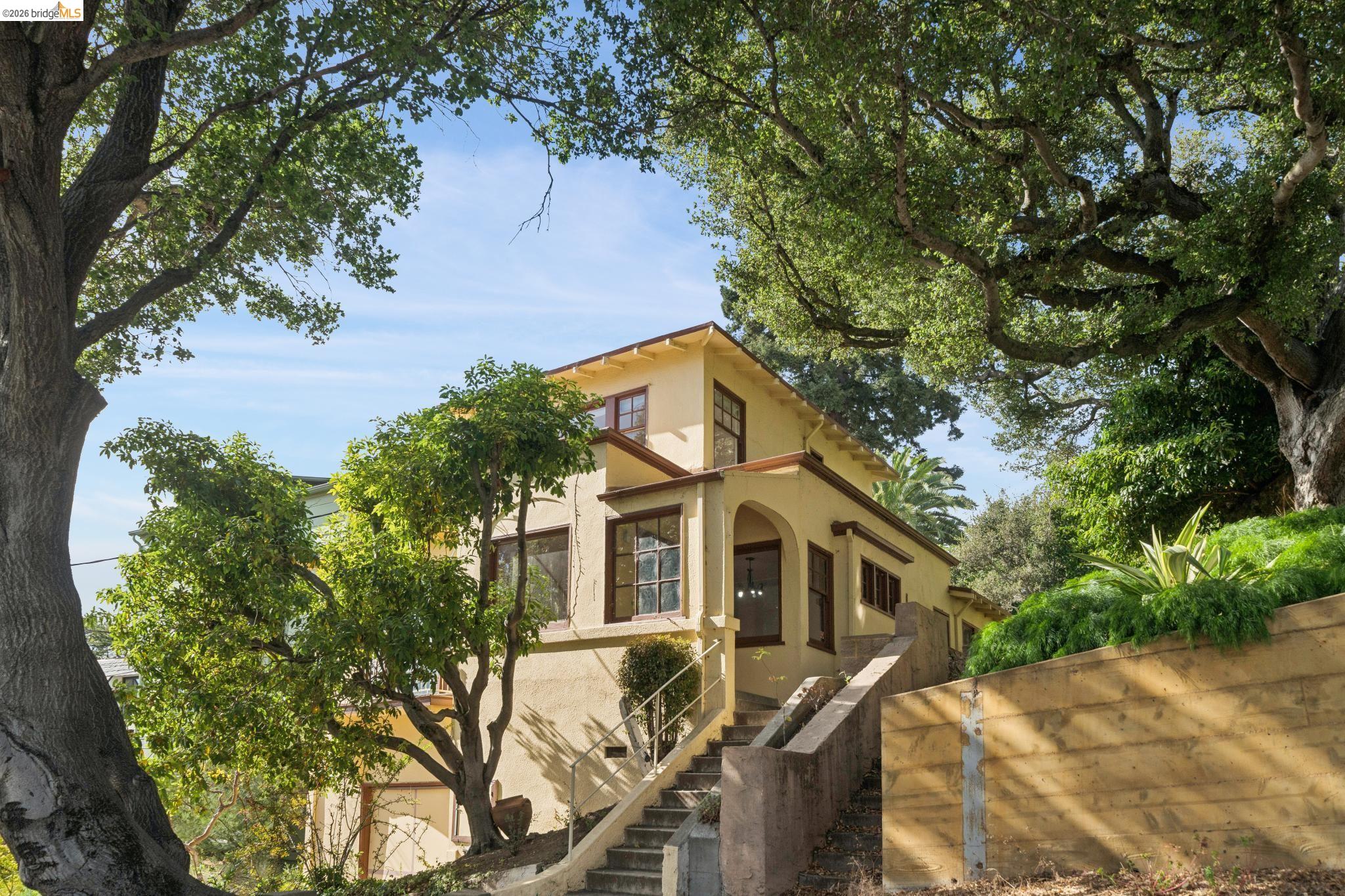 Yellow stucco home with dark wood trim, exterior stairs, and mature trees.