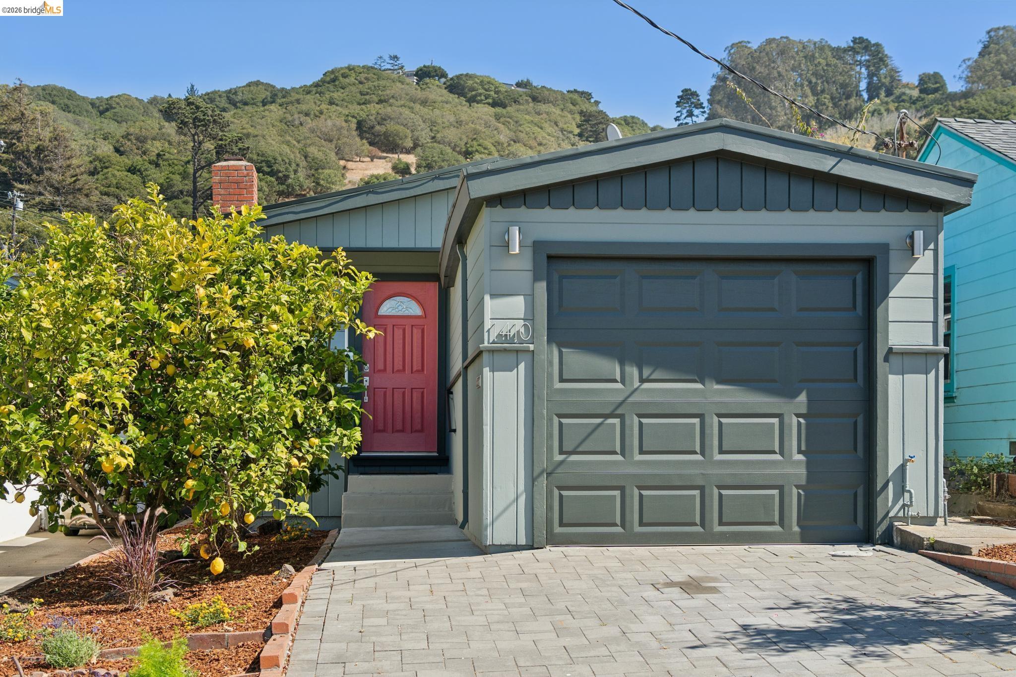 Gray home with a dark garage door, red front door, and lemon tree in the front garden.