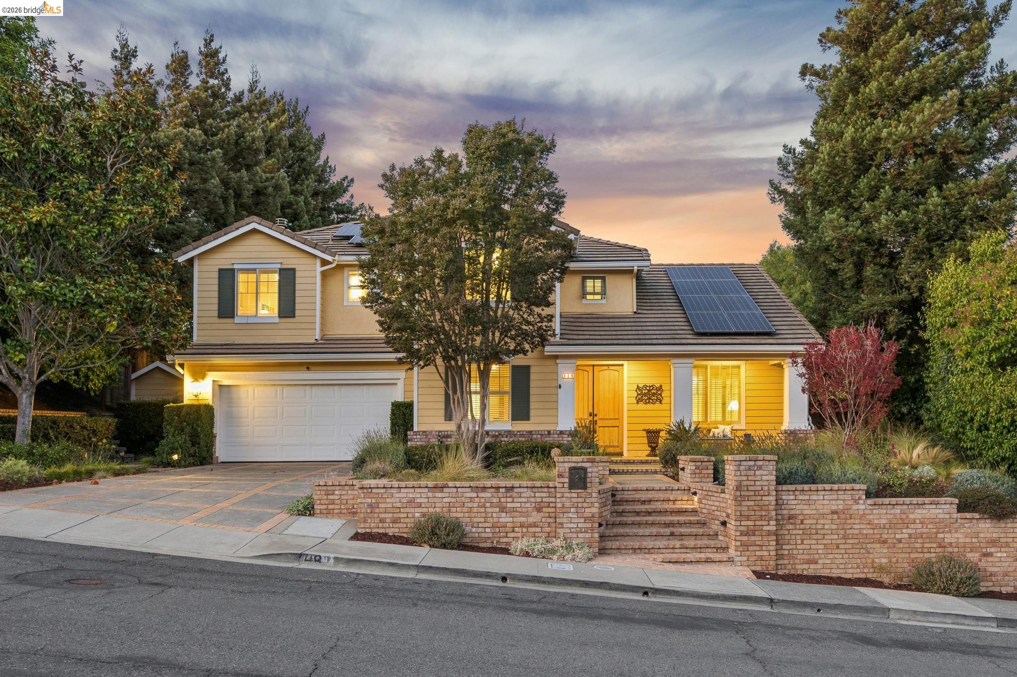 Two-story tan home at dusk with solar panels, a double garage, and a brick front wall.