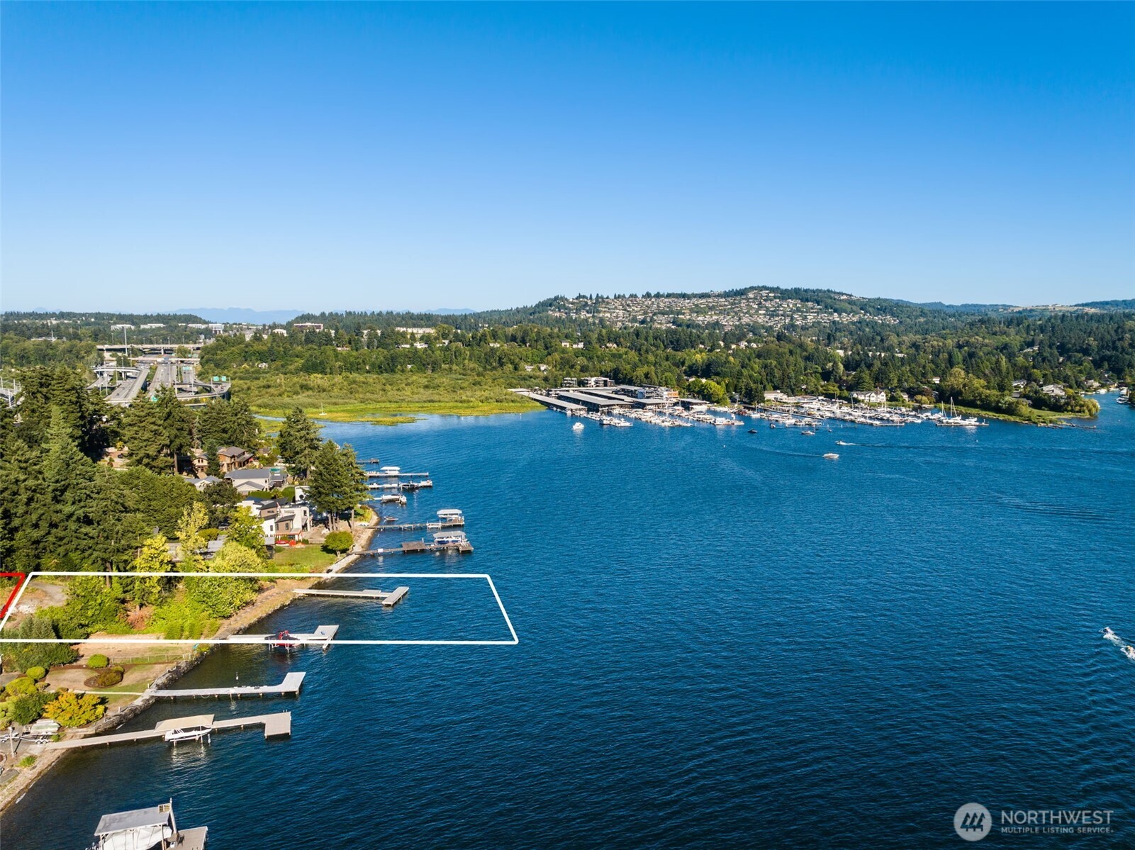 Aerial waterfront lot outlined along a wooded shoreline, with a private dock and marina across the lake.