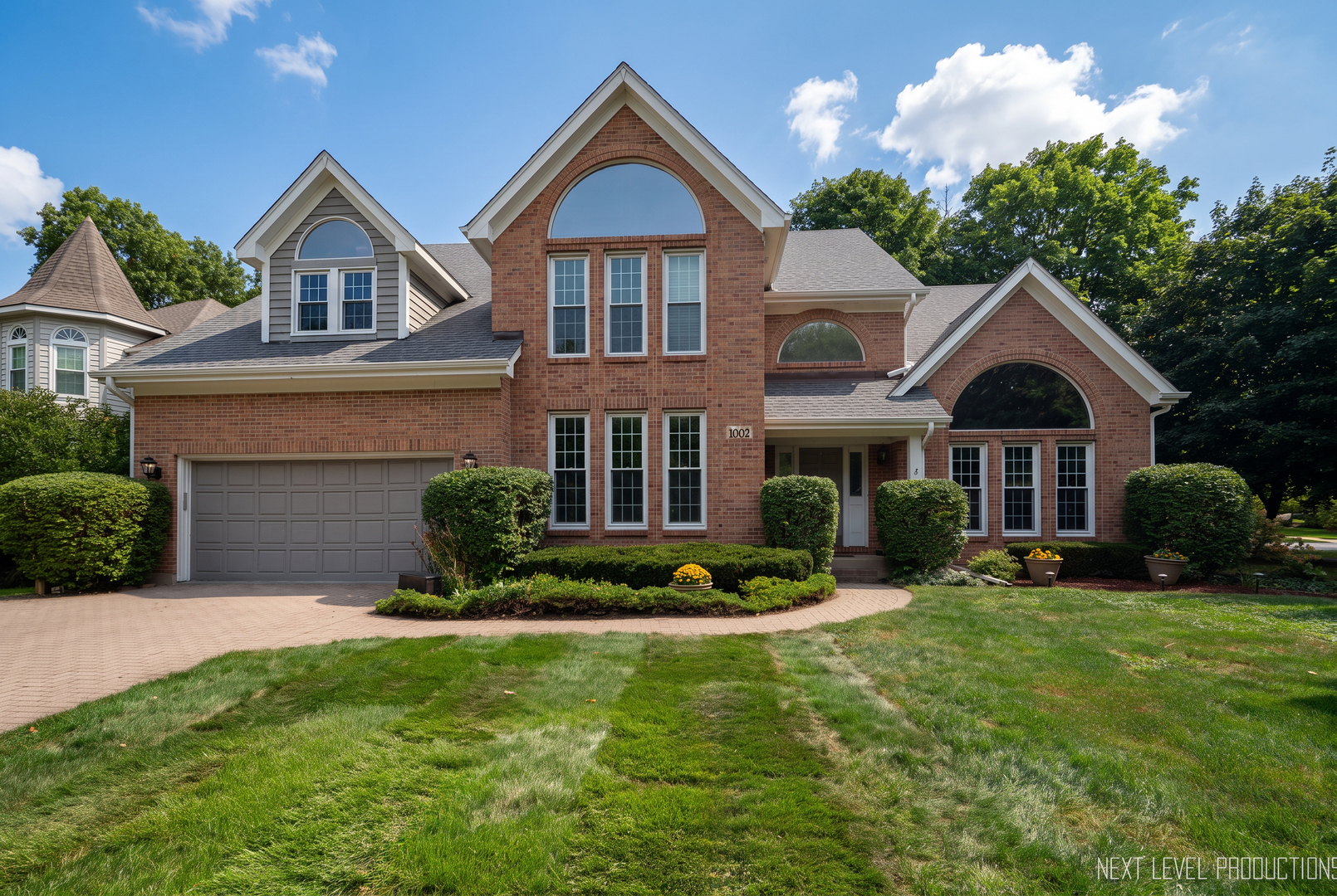 Two-story brick house with arched windows, an attached garage, and landscaped front lawn.