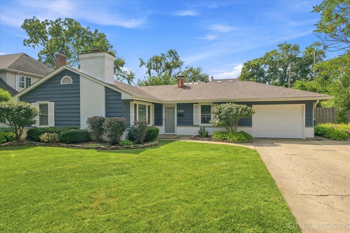 Blue single-story house with a white chimney, attached garage, and broad green front lawn.