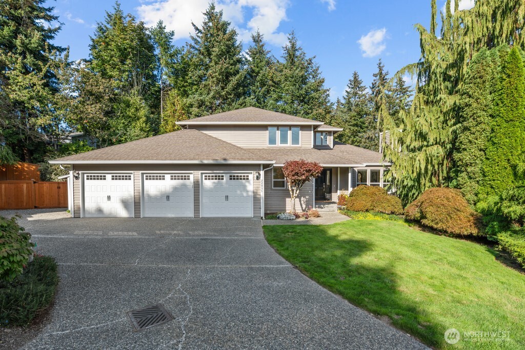Two-story gray house with three garage doors, a broad driveway, and landscaped lawn.
