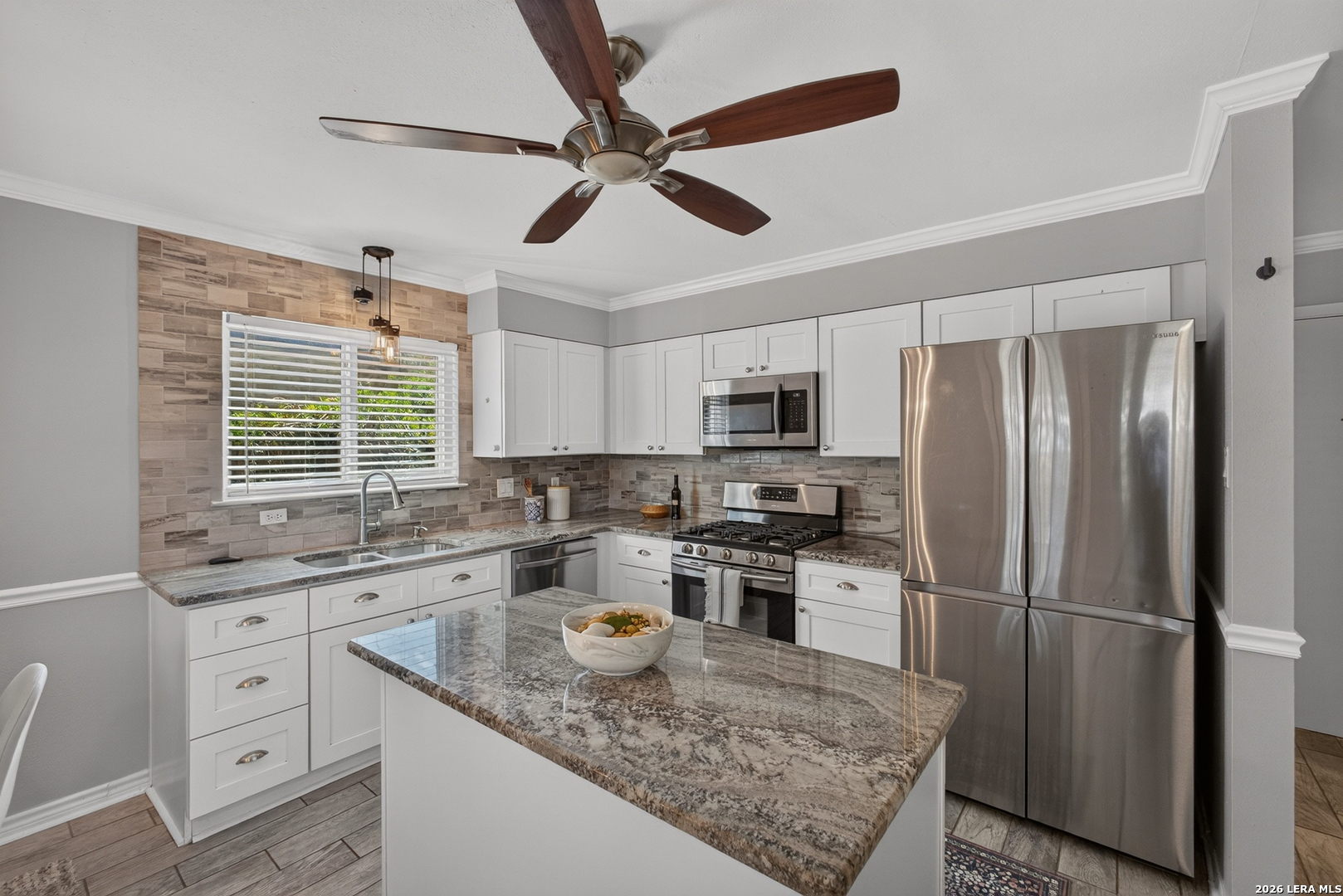 Kitchen with white cabinets, granite island, stainless steel appliances, and a tiled backsplash.