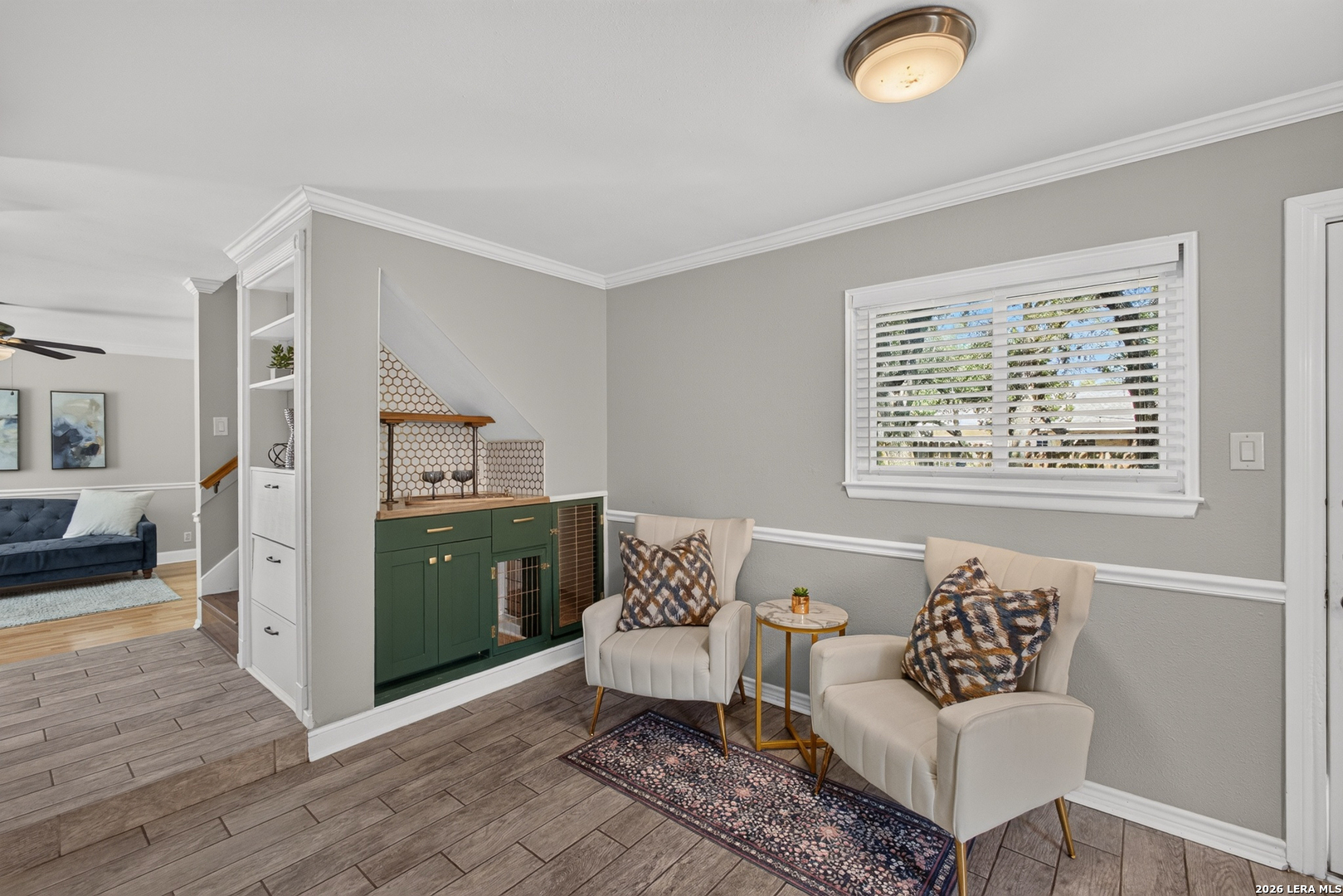 Sitting area with two cream chairs beside a green built-in cabinet and tiled hearth.
