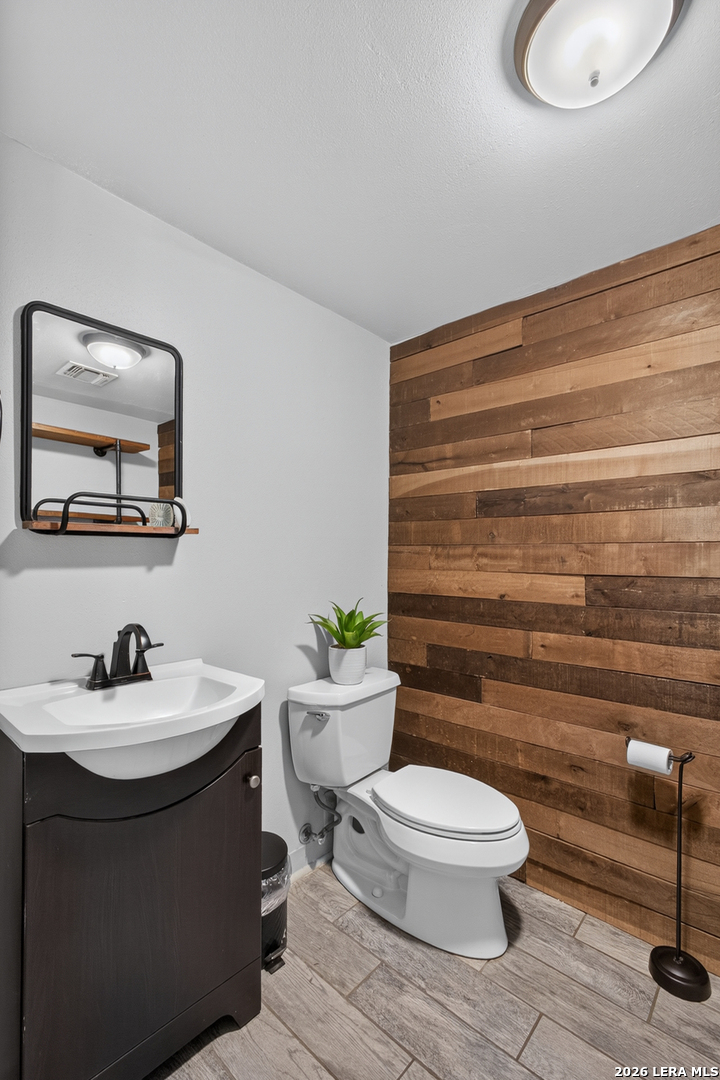 Bathroom with a wood-plank accent wall, white toilet, and dark vanity.