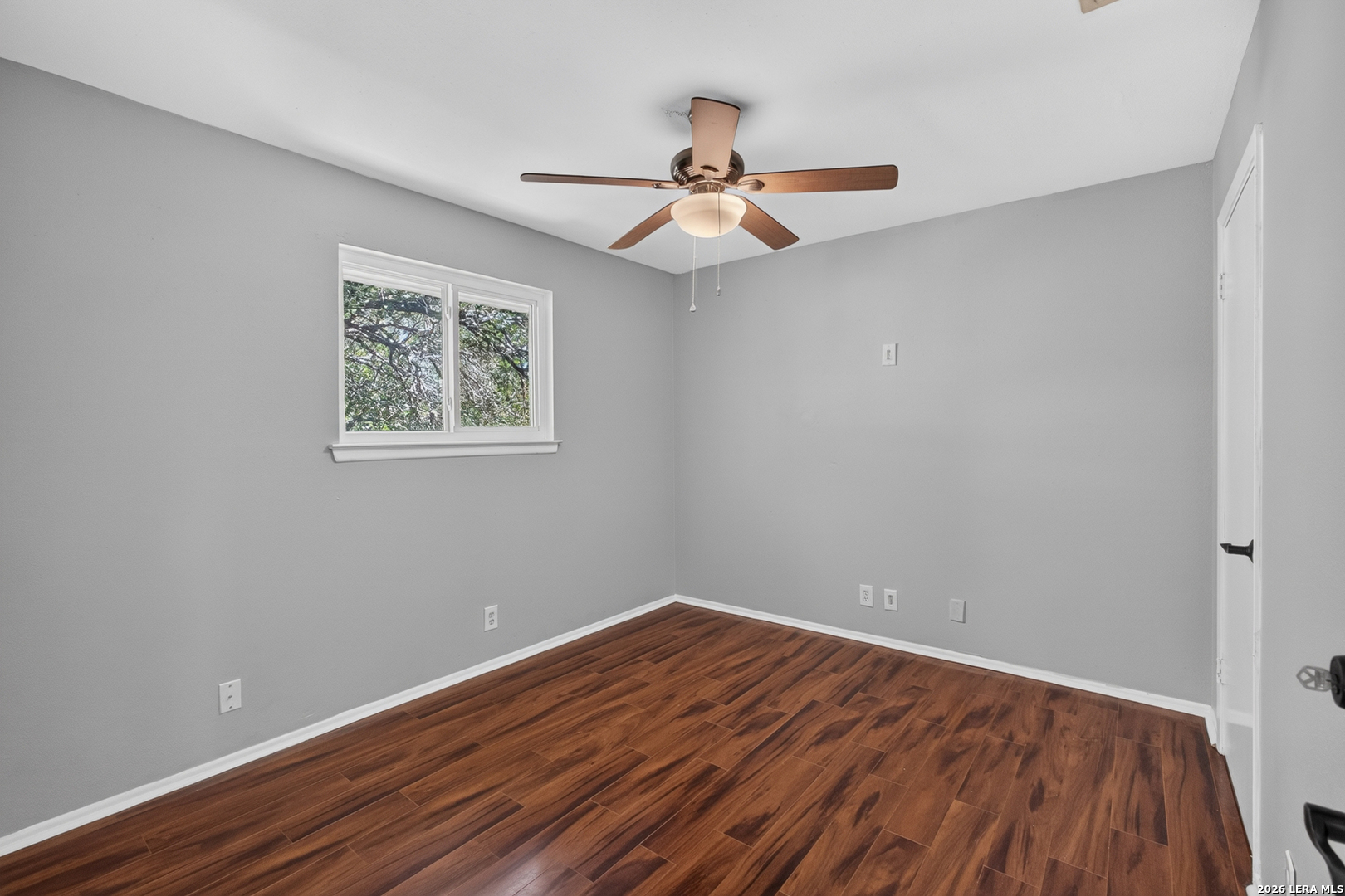 Empty room with wood-look flooring, gray walls, a window, and ceiling fan