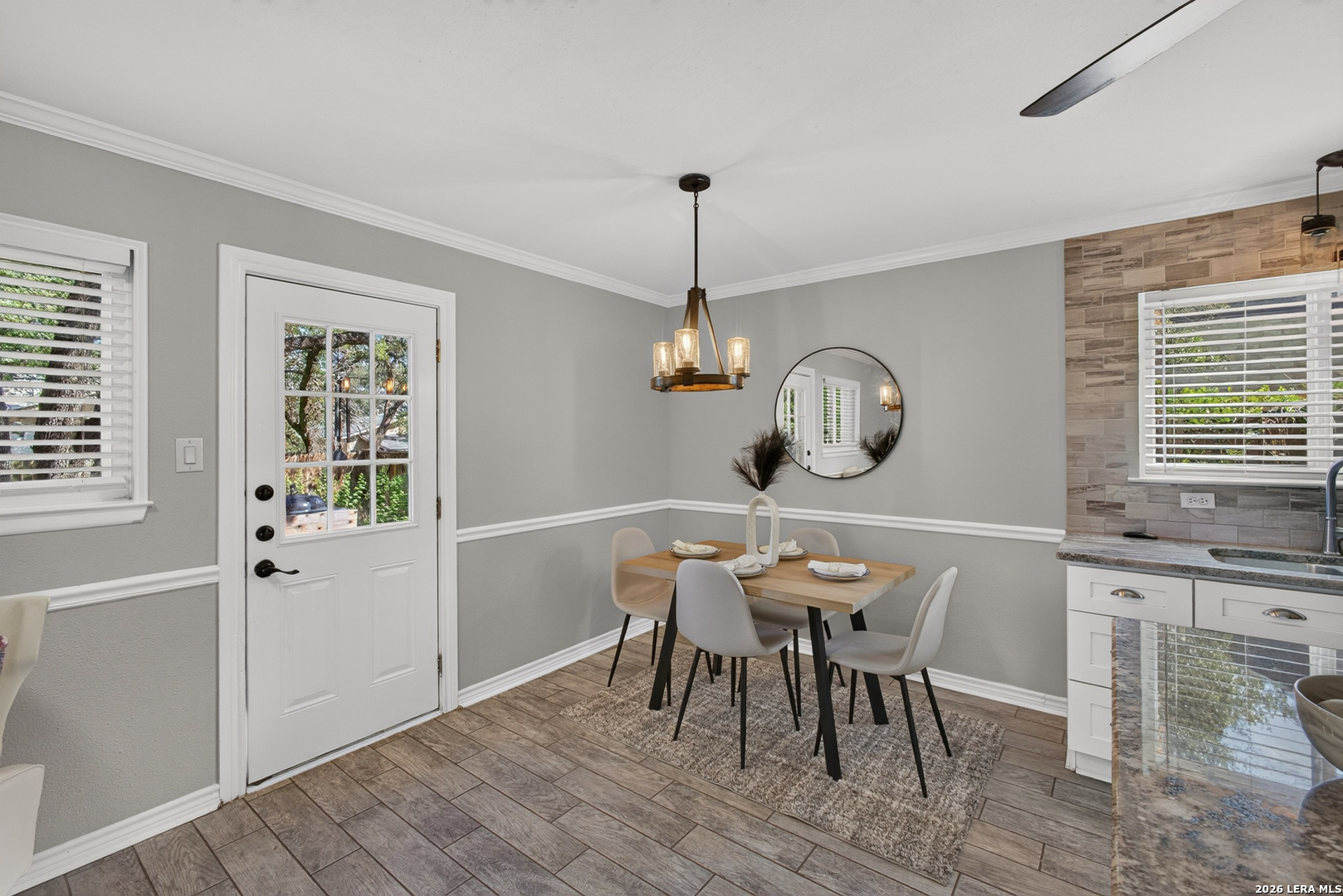 Dining area with a wood table beside a glass-paneled door and tiled kitchen wall.
