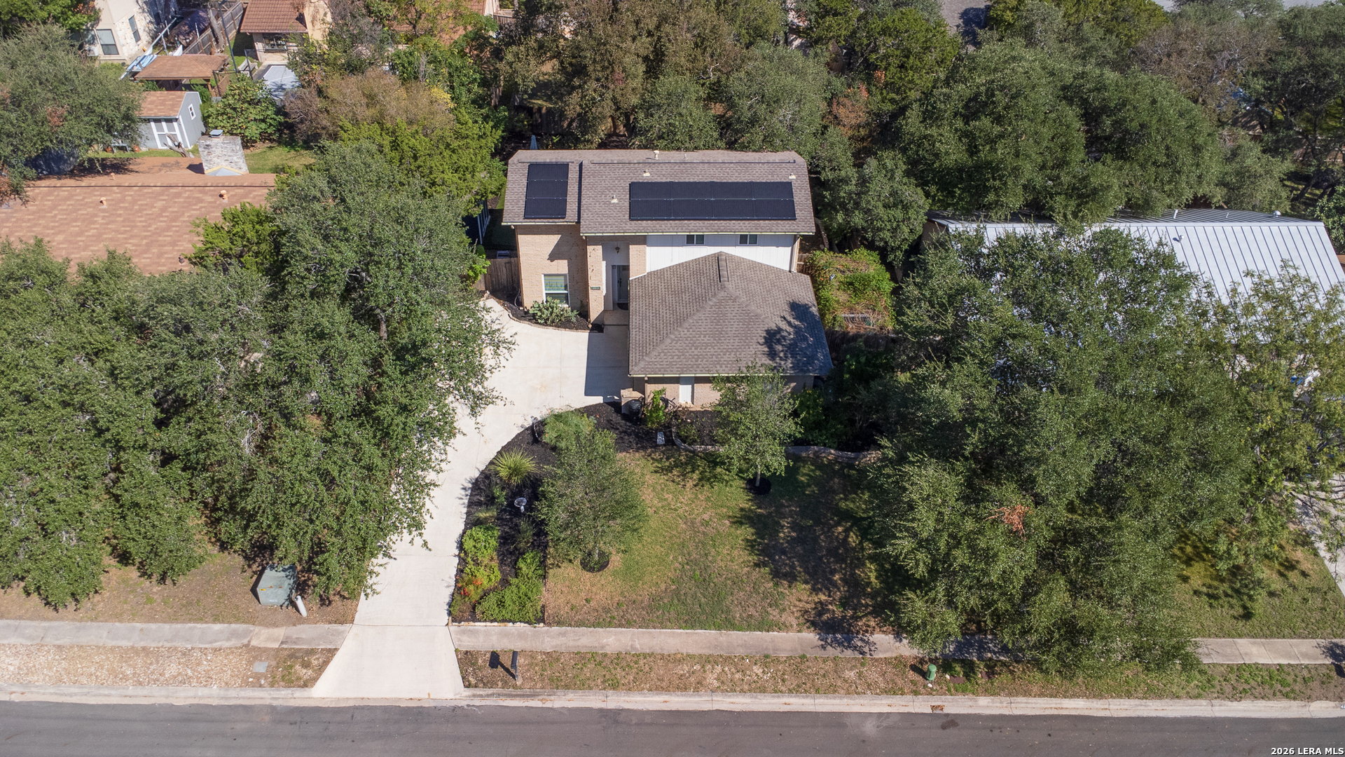 Aerial view of a two-story brick home with rooftop solar panels and a curved driveway.