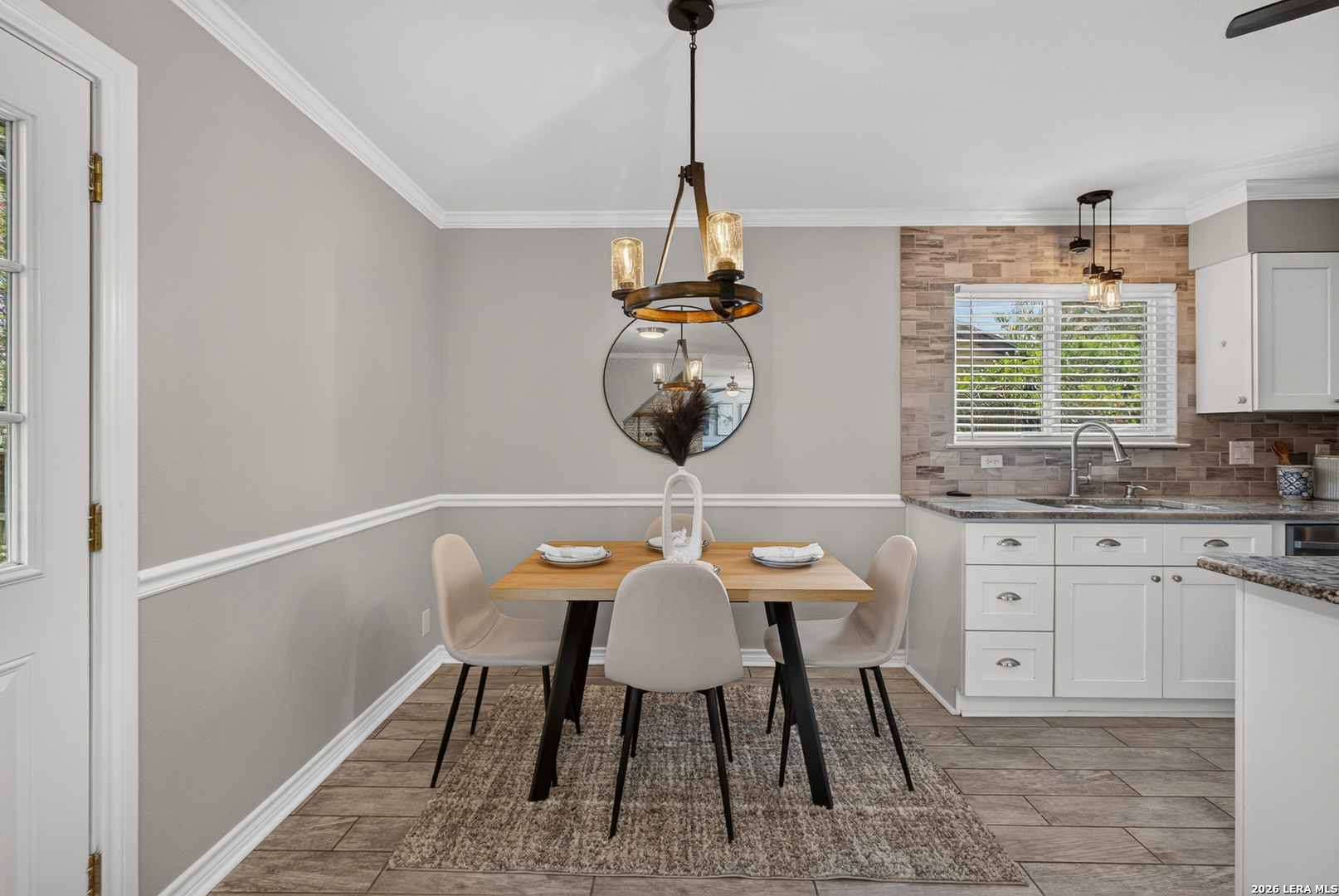Dining area with a set table beside a white-cabinet kitchen and stone-tile backsplash.
