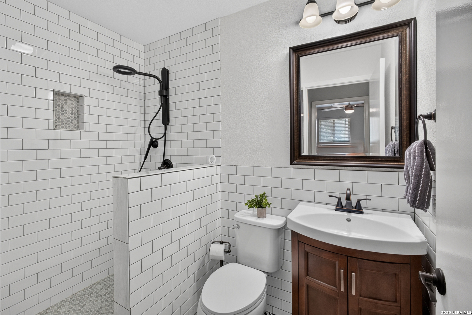 Bathroom with a white subway-tile shower, black fixtures, and a dark wood vanity.