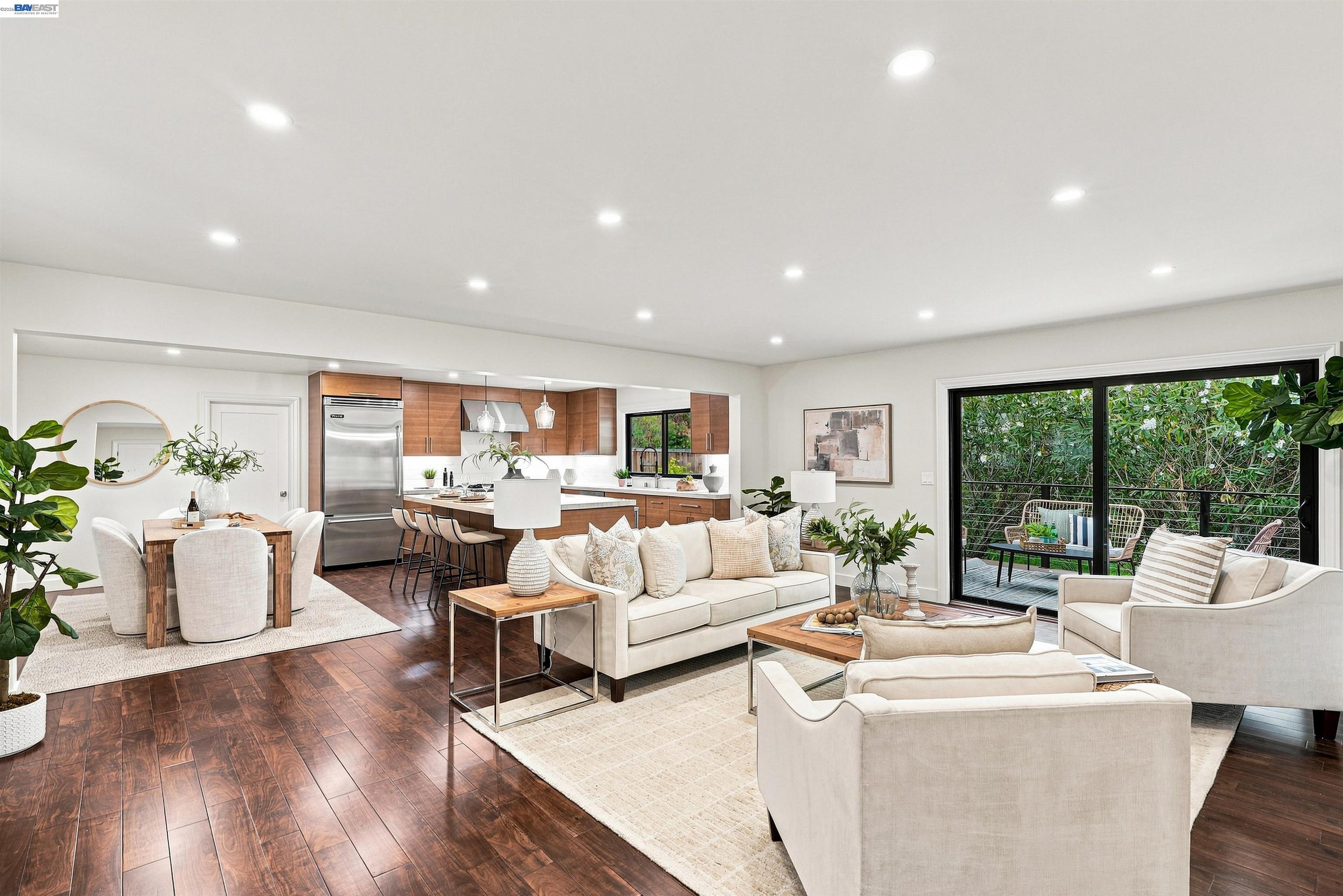 Open-plan living room and kitchen with warm wood cabinetry and sliding doors to a leafy deck.