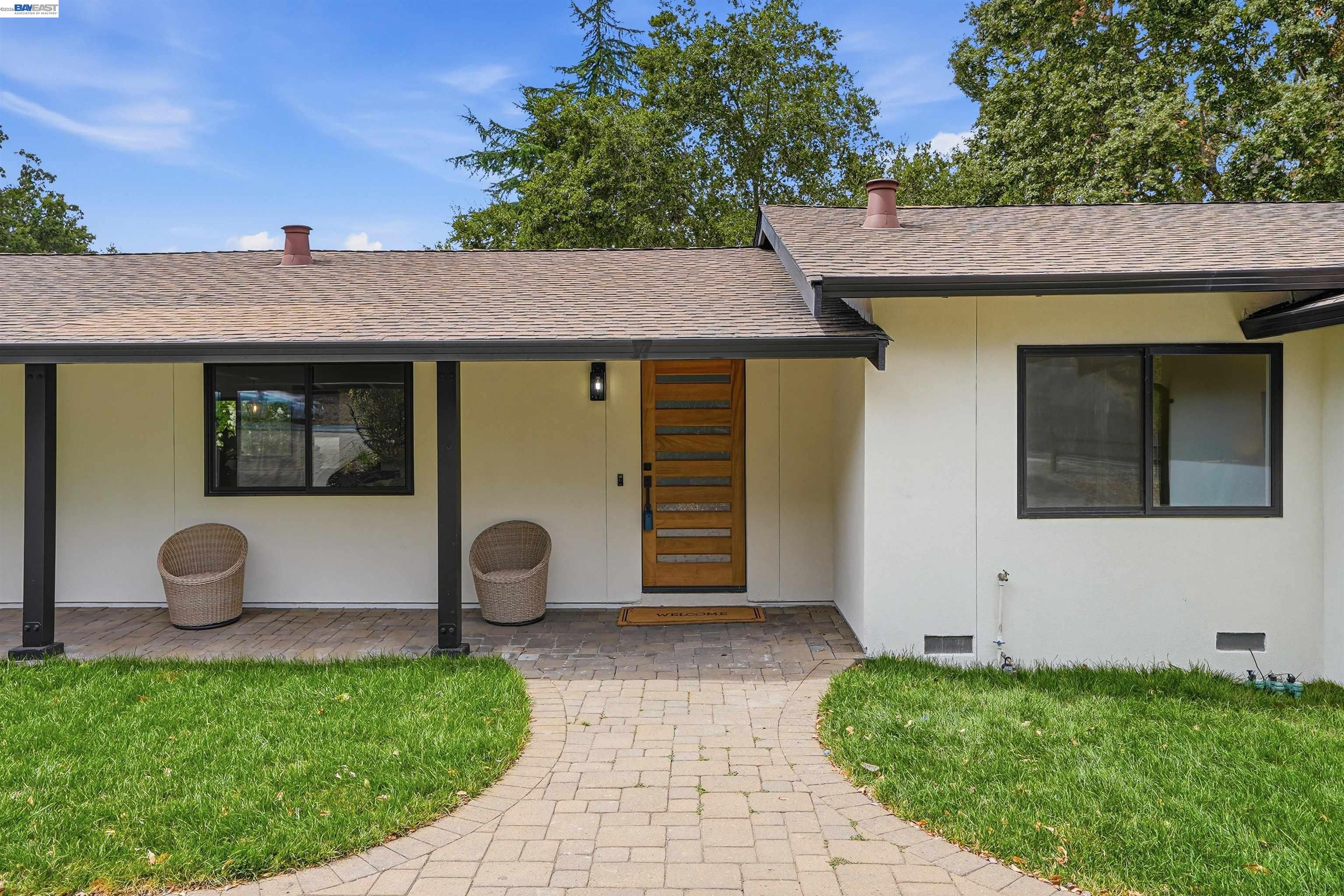 Single-story home entrance with covered porch, wood front door, and curved paver walkway.