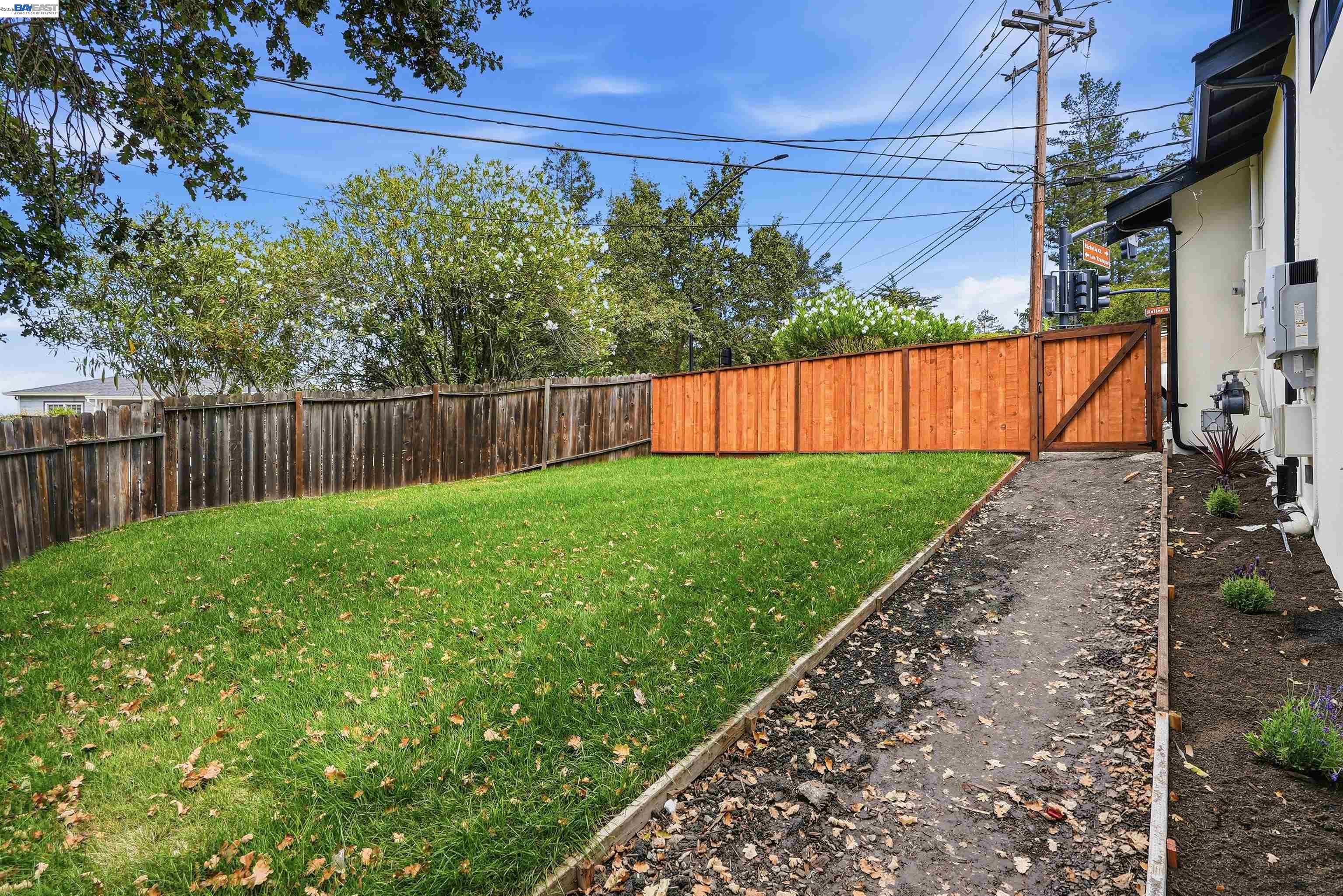 Fenced backyard with a green lawn, mature trees, and a warm-toned wooden gate.