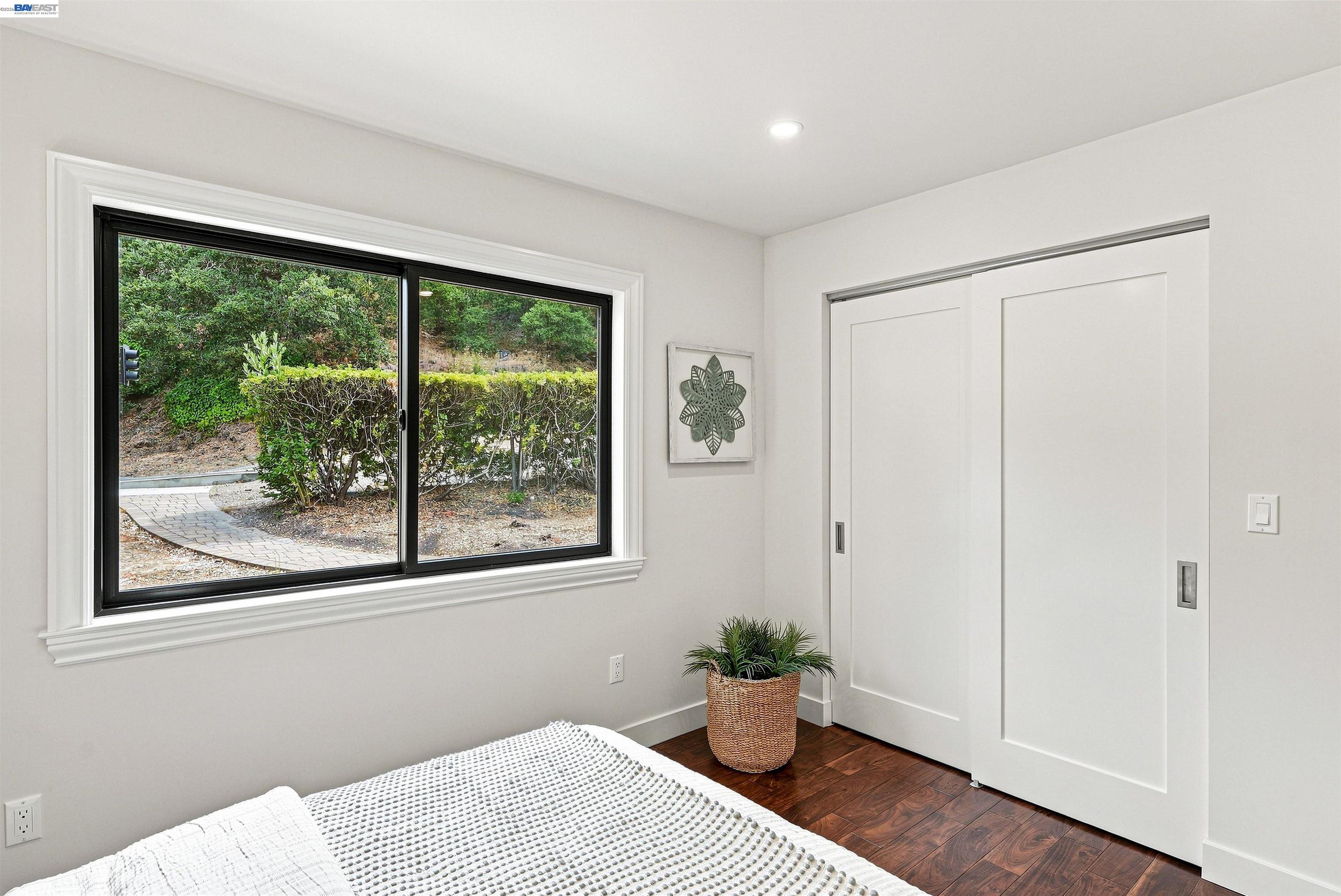 Bedroom with a large window overlooking landscaped greenery and white sliding closet doors.