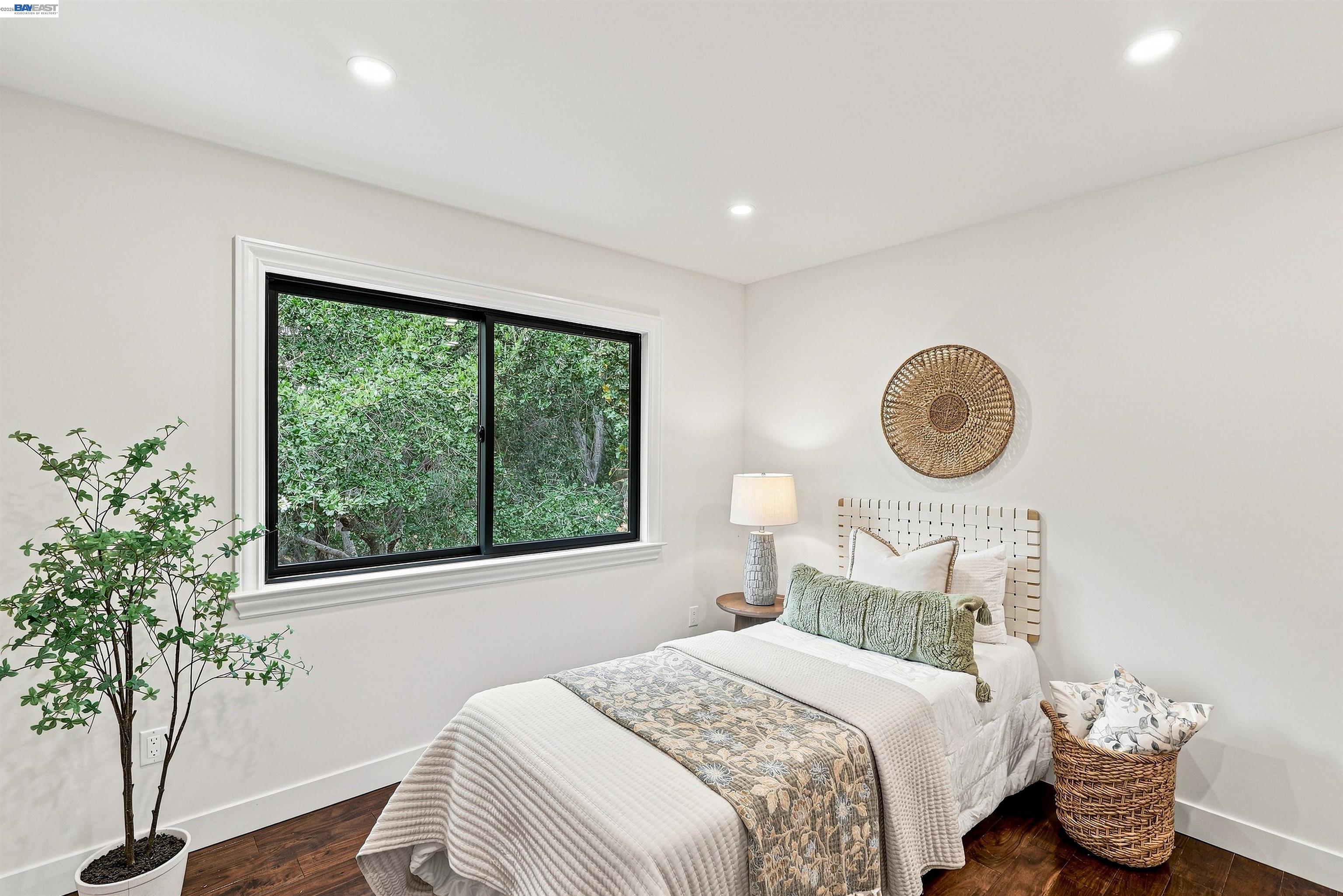 Staged bedroom with a white bed, woven headboard, and large window overlooking greenery.