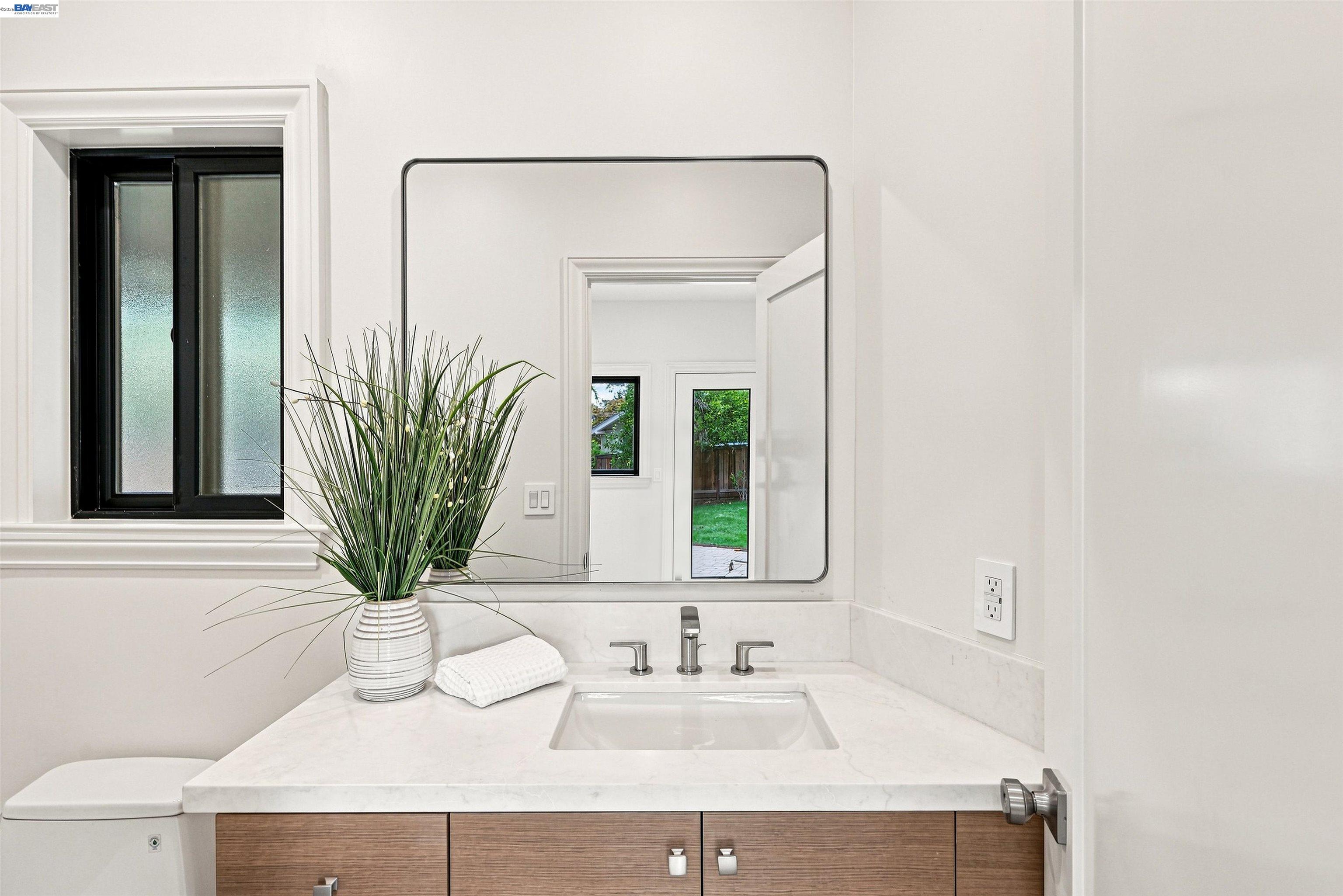 Bathroom vanity with a stone counter, wood-grain cabinets, large mirror, and potted plant.
