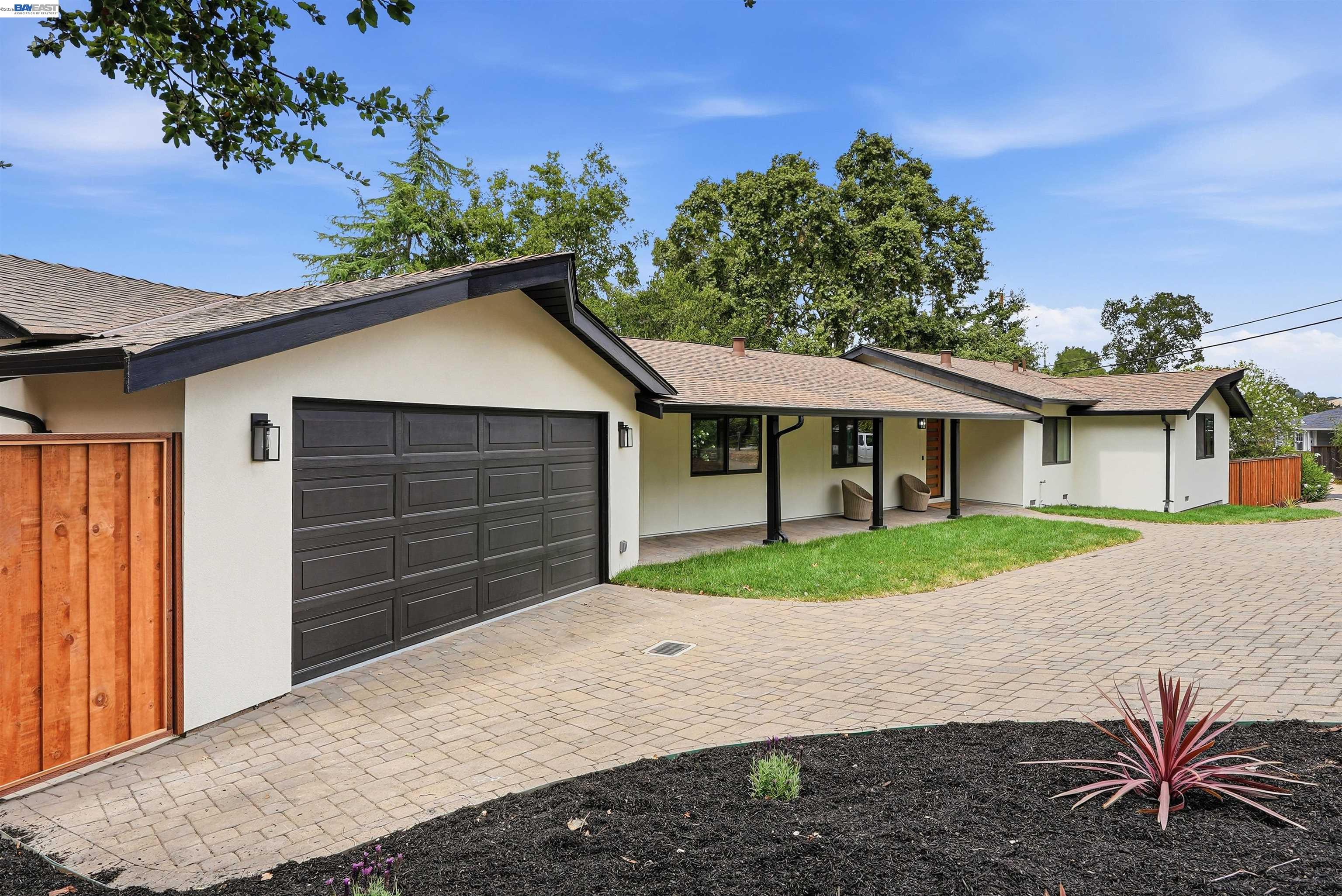 Single-story white home with dark trim, a large garage, covered entry, and landscaped paved driveway.