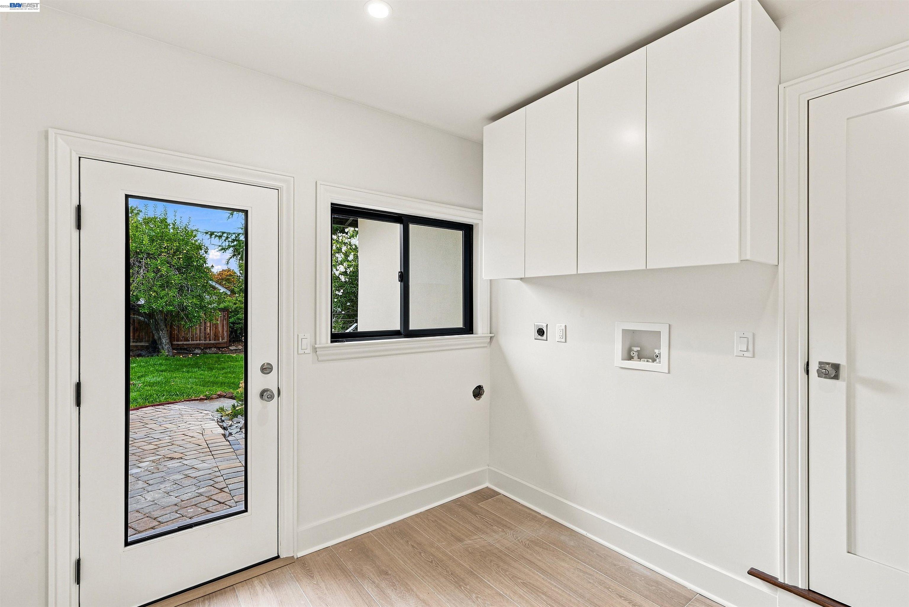 Vacant laundry room with white cabinets, appliance hookups, and a glass door to the backyard.