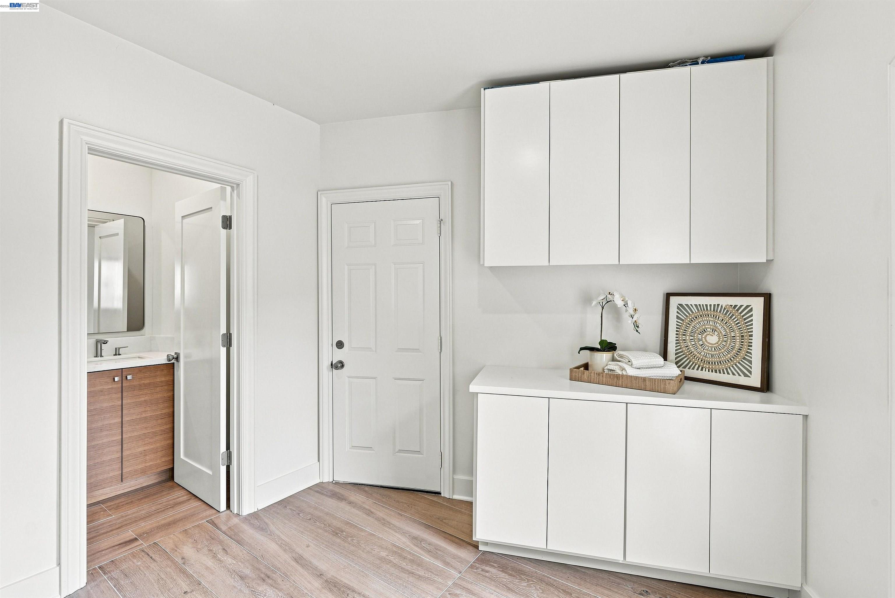 Entryway with white storage cabinets, wood-look tile flooring, and an open doorway to a bathroom.