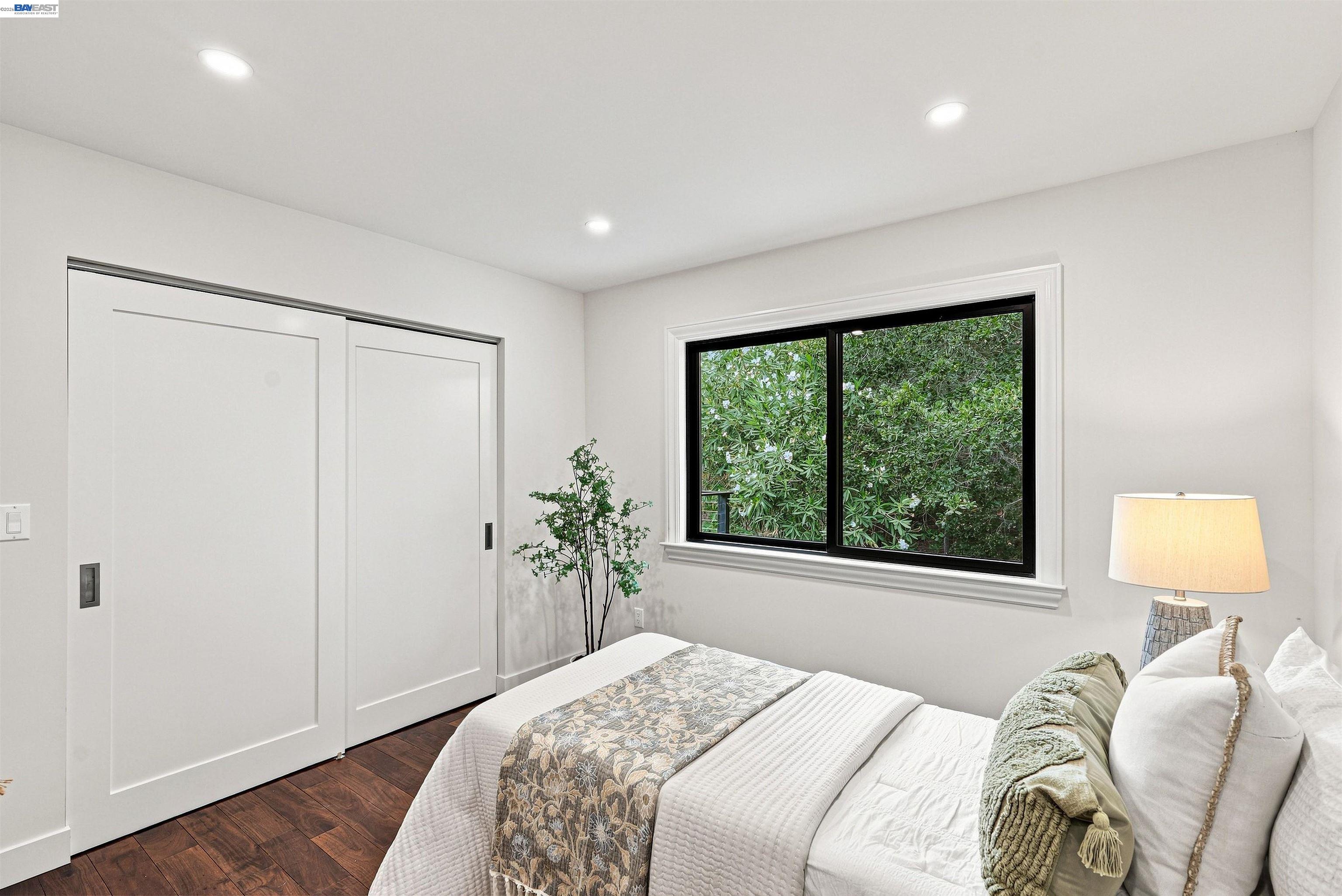 Staged bedroom with a white bed, sliding closet doors, and a window overlooking greenery.