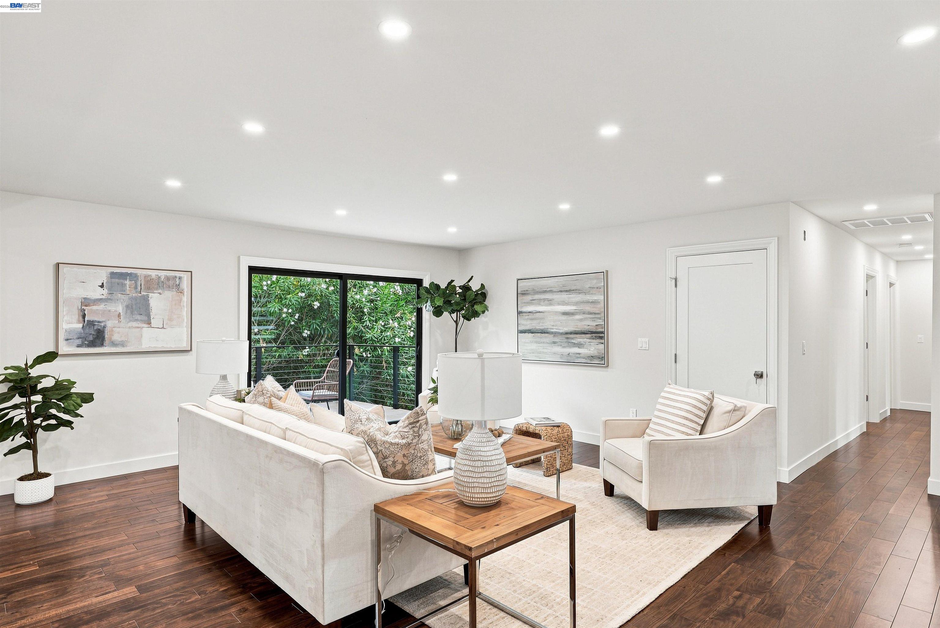 Staged living room with white seating, dark hardwood floors, and sliding glass doors facing greenery.