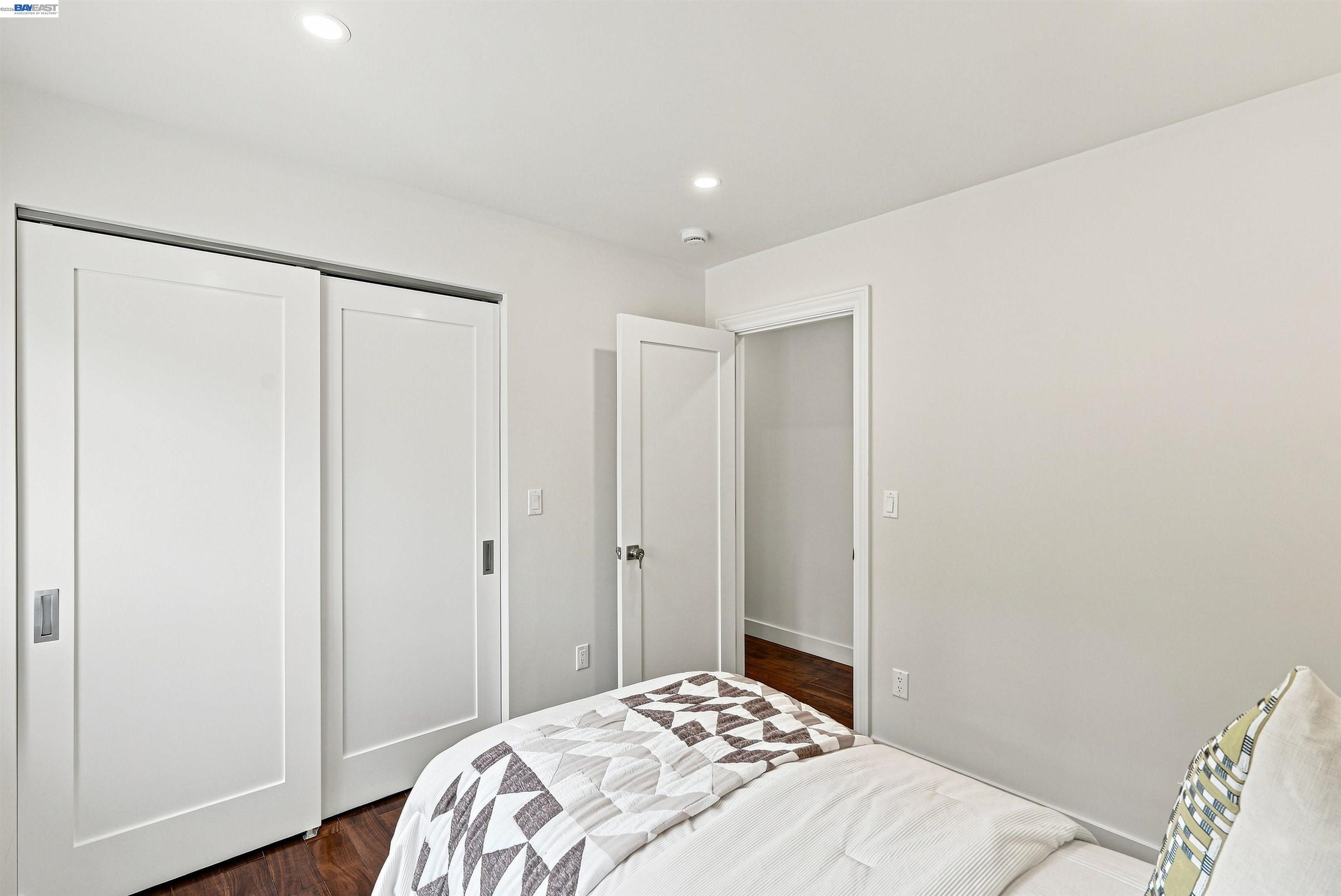 Bedroom with a geometric quilt, white sliding closet doors, and dark hardwood floors.