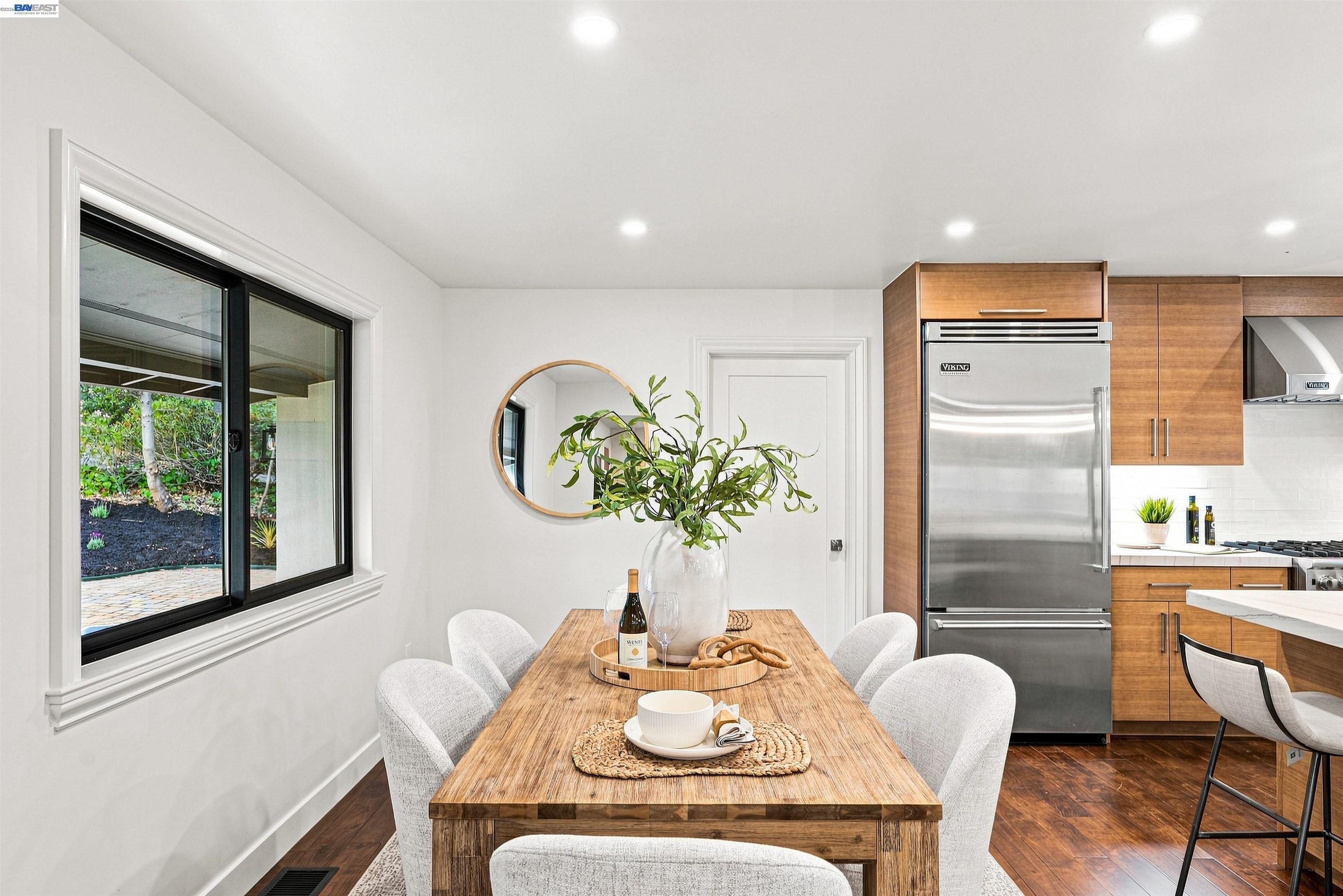 Kitchen dining area with a wood table, warm cabinetry, stainless steel appliances, and a garden view.