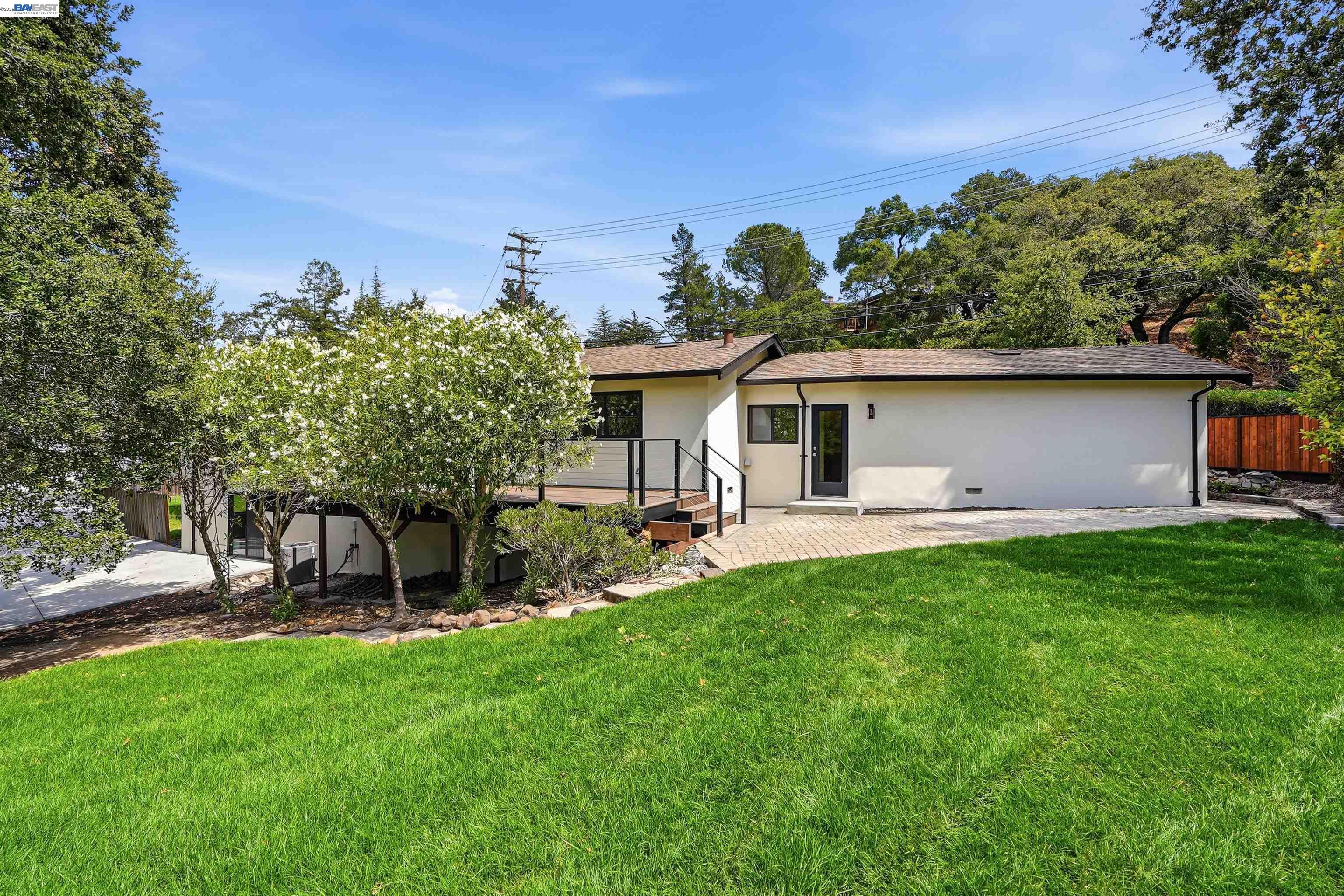Rear exterior of a white single-story home with a raised deck, paved patio, and lawn.