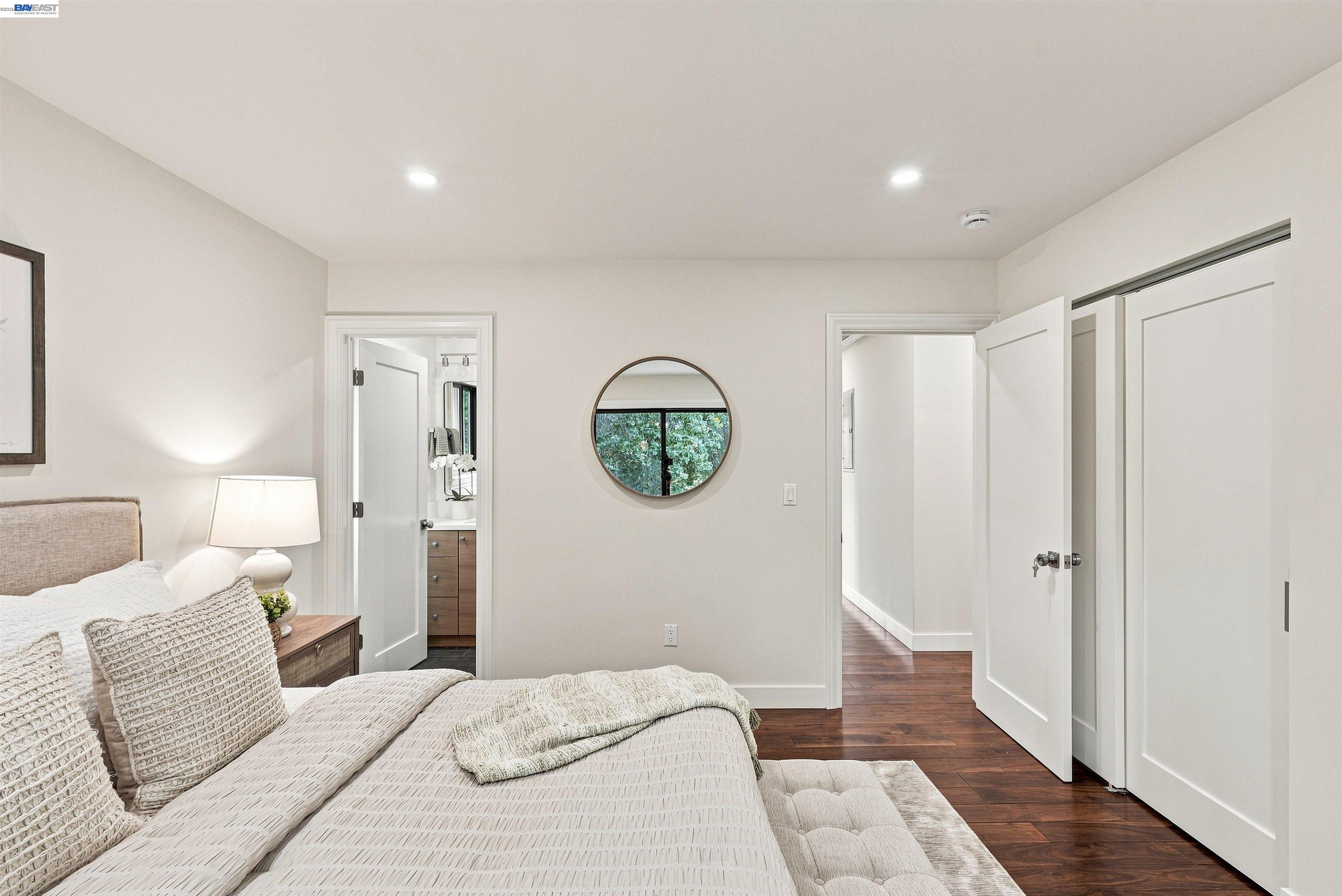 Staged bedroom with textured white bedding, a round wall mirror, and dark wood floors.
