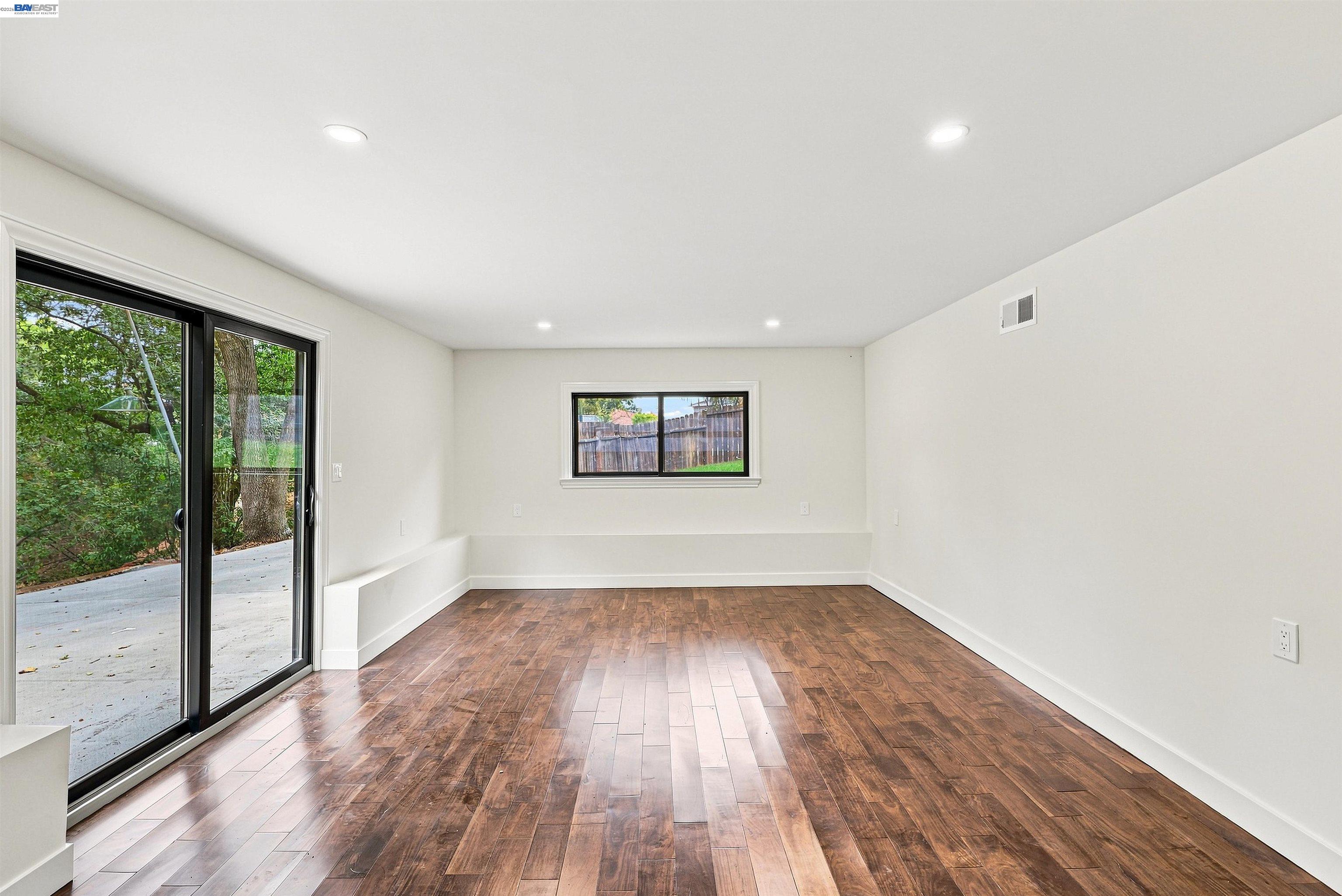 Empty room with dark wood floors, a sliding glass door, and a window facing the yard.