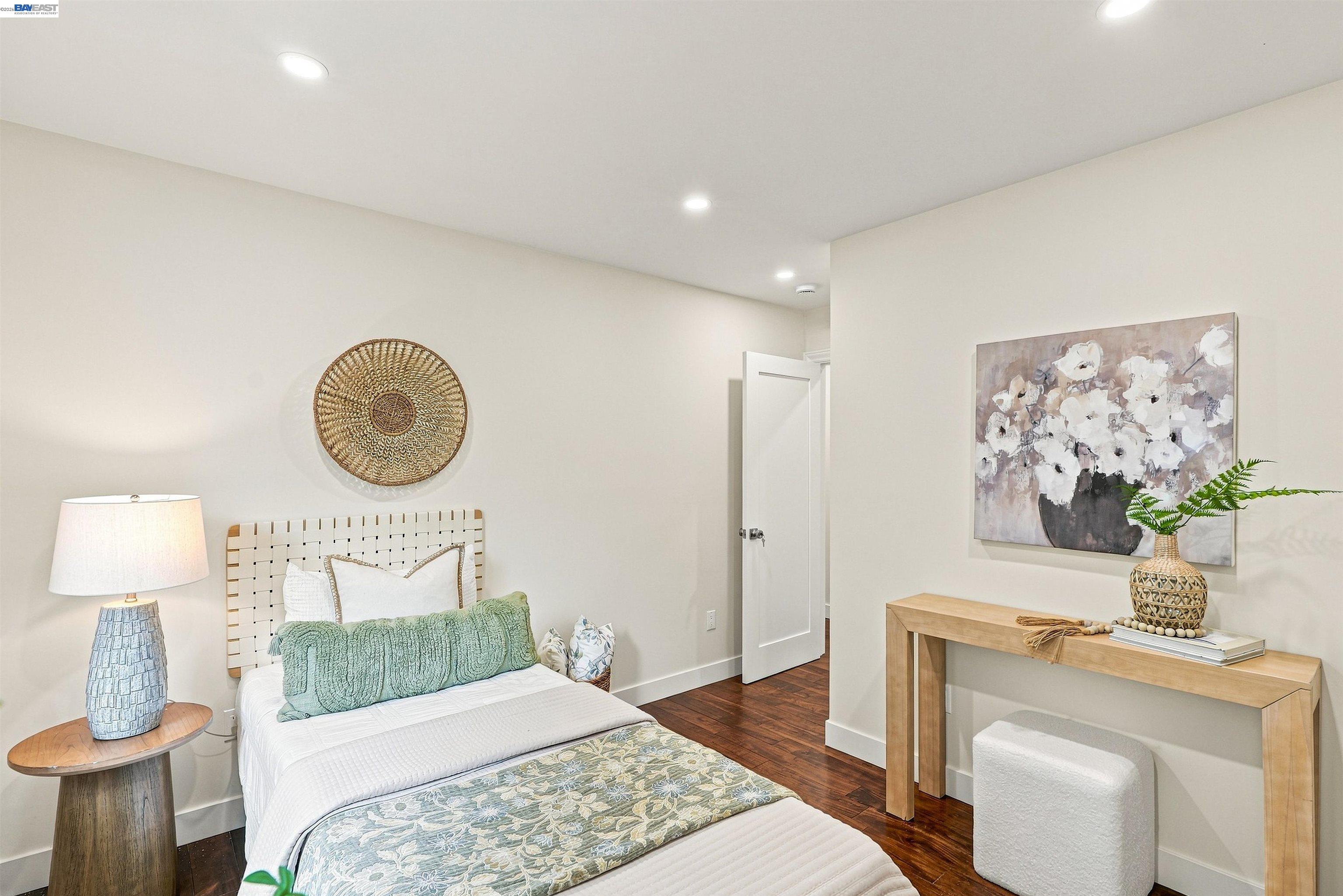 Staged bedroom with a white bed, pale green pillows, woven headboard, and floral artwork.